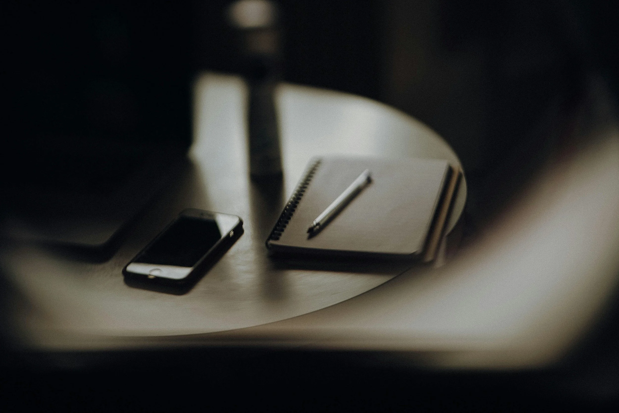 A notebook with a pen, a smartphone, and a laptop on a wooden table.