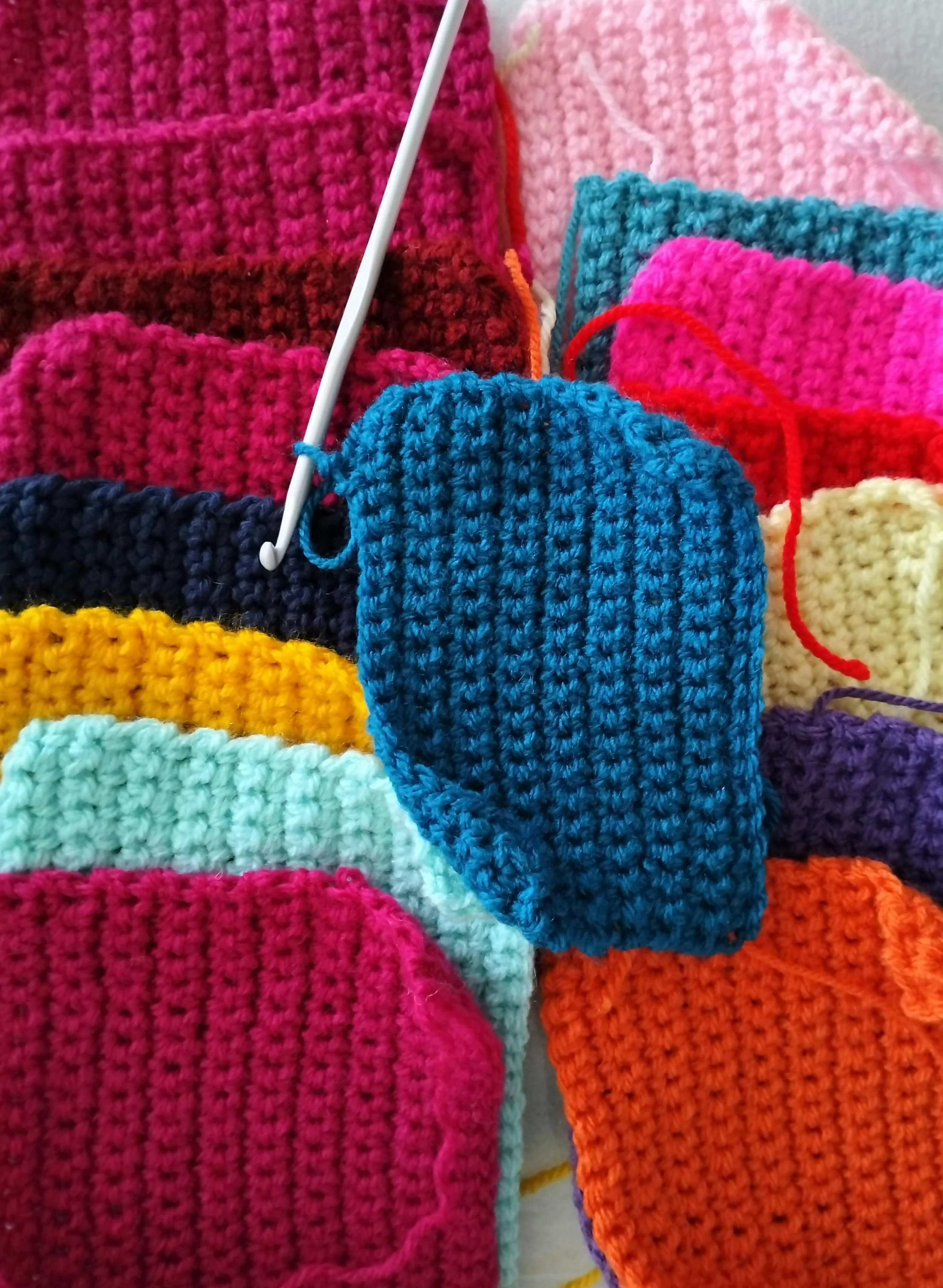 Colorful, small, hand-knitted crochet squares in pink, blue, yellow, orange, purple, teal, white, black, maroon, and cream colors, arranged in a pile.