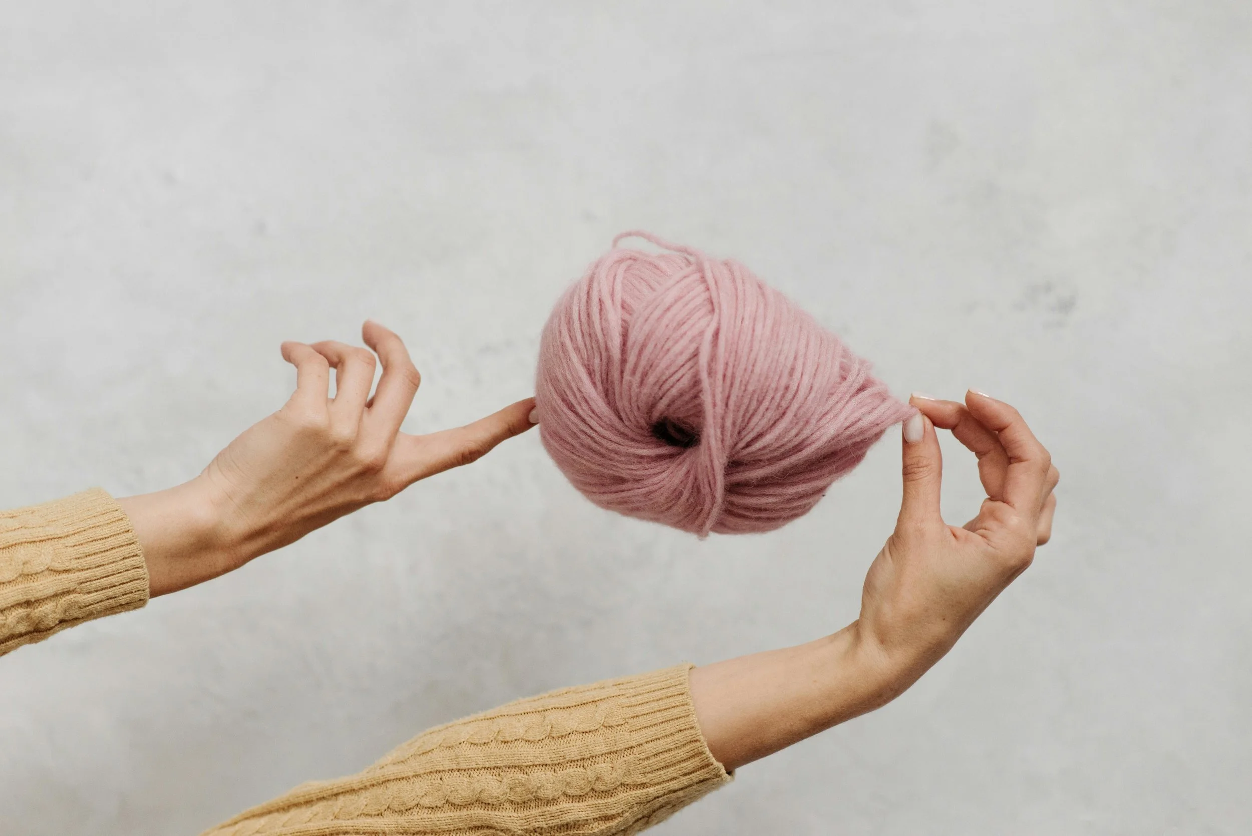 Hands holding a ball of pink yarn against a neutral background.
