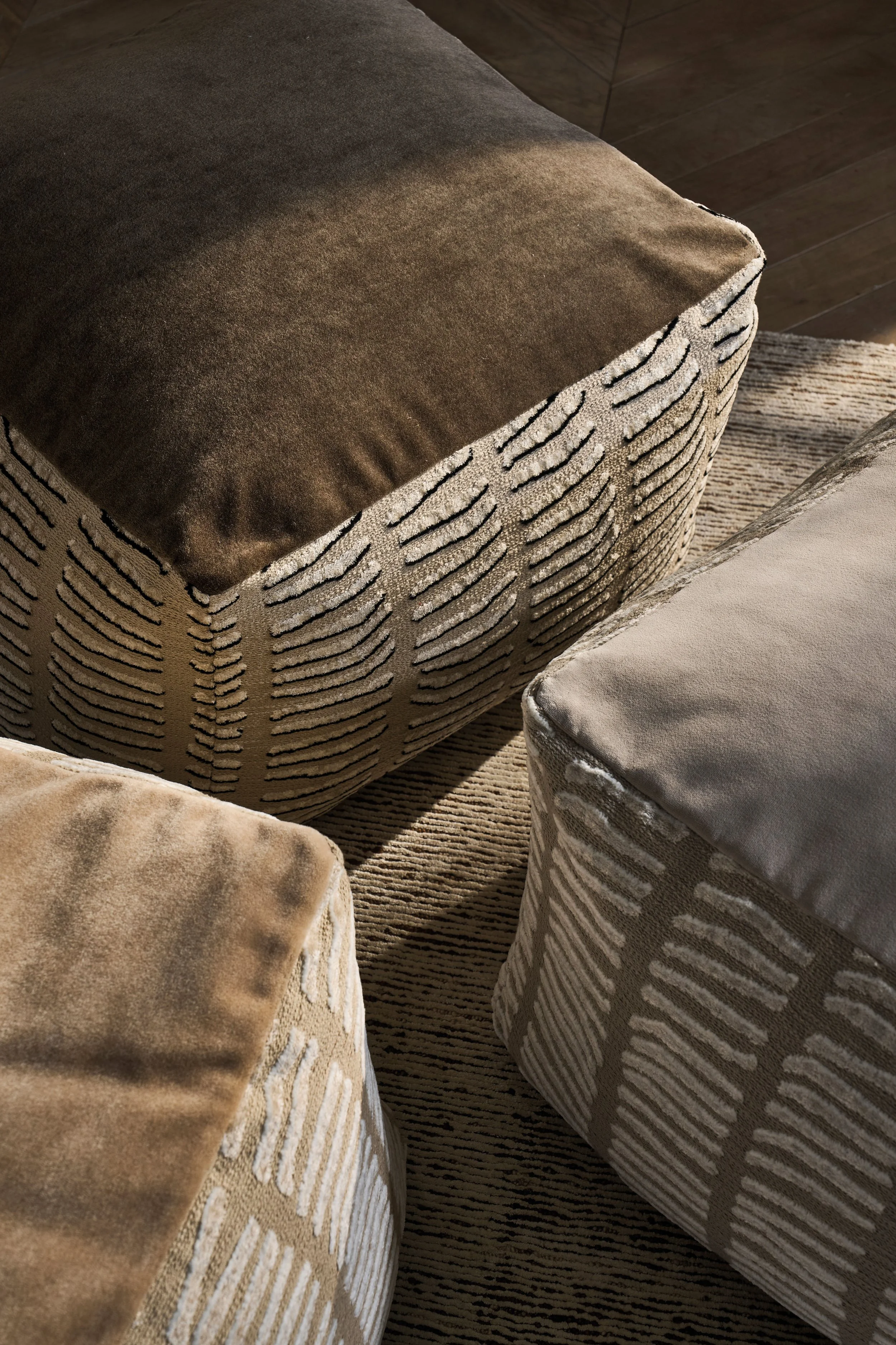 Close-up of four upholstered ottomans with patterned fabric, arranged on a striped rug, in a living room setting.