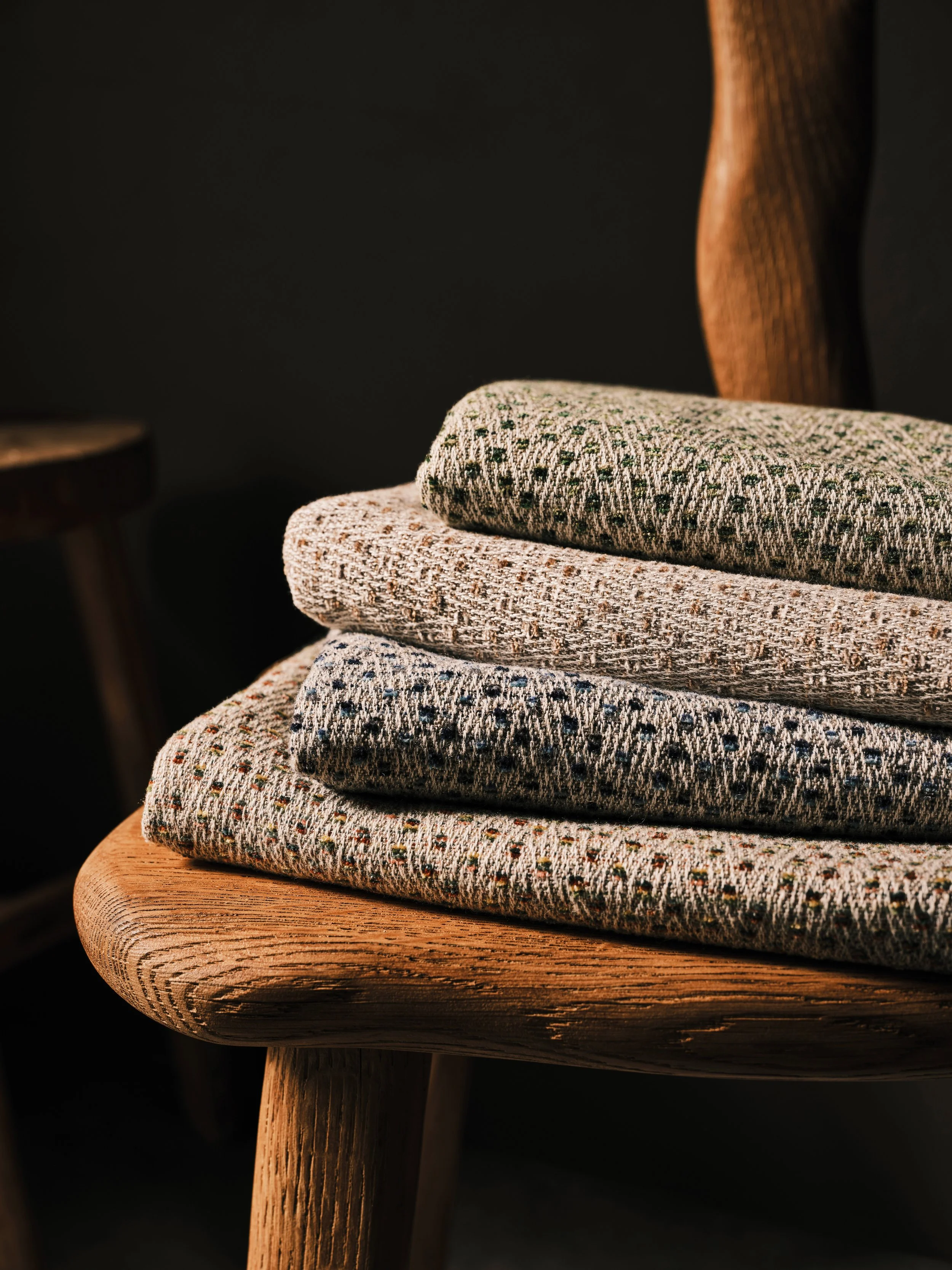 Stack of three folded patterned fabric pieces on a wooden chair with a dark background.