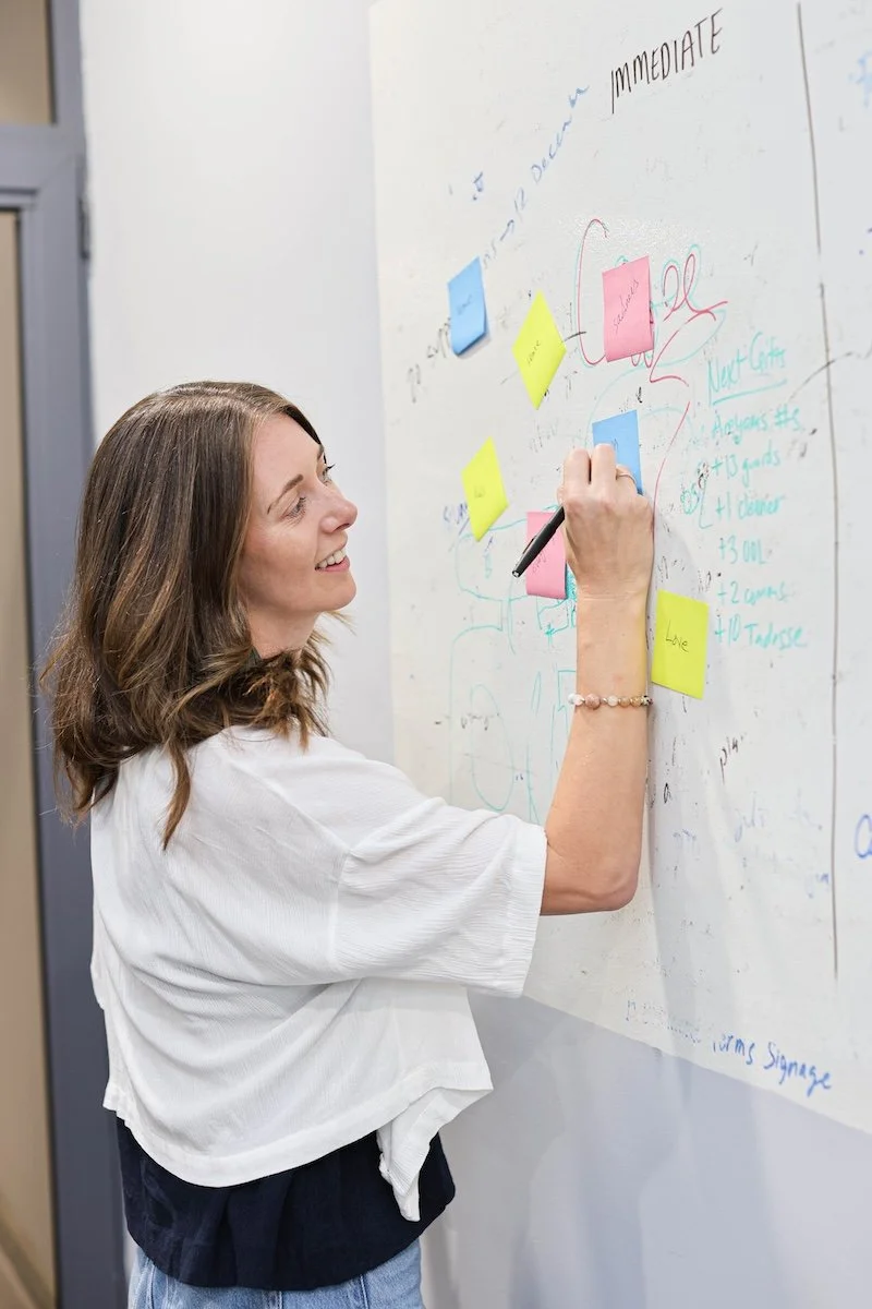 Ellie writing on a whiteboard filled with colorful sticky notes and handwritten notes.