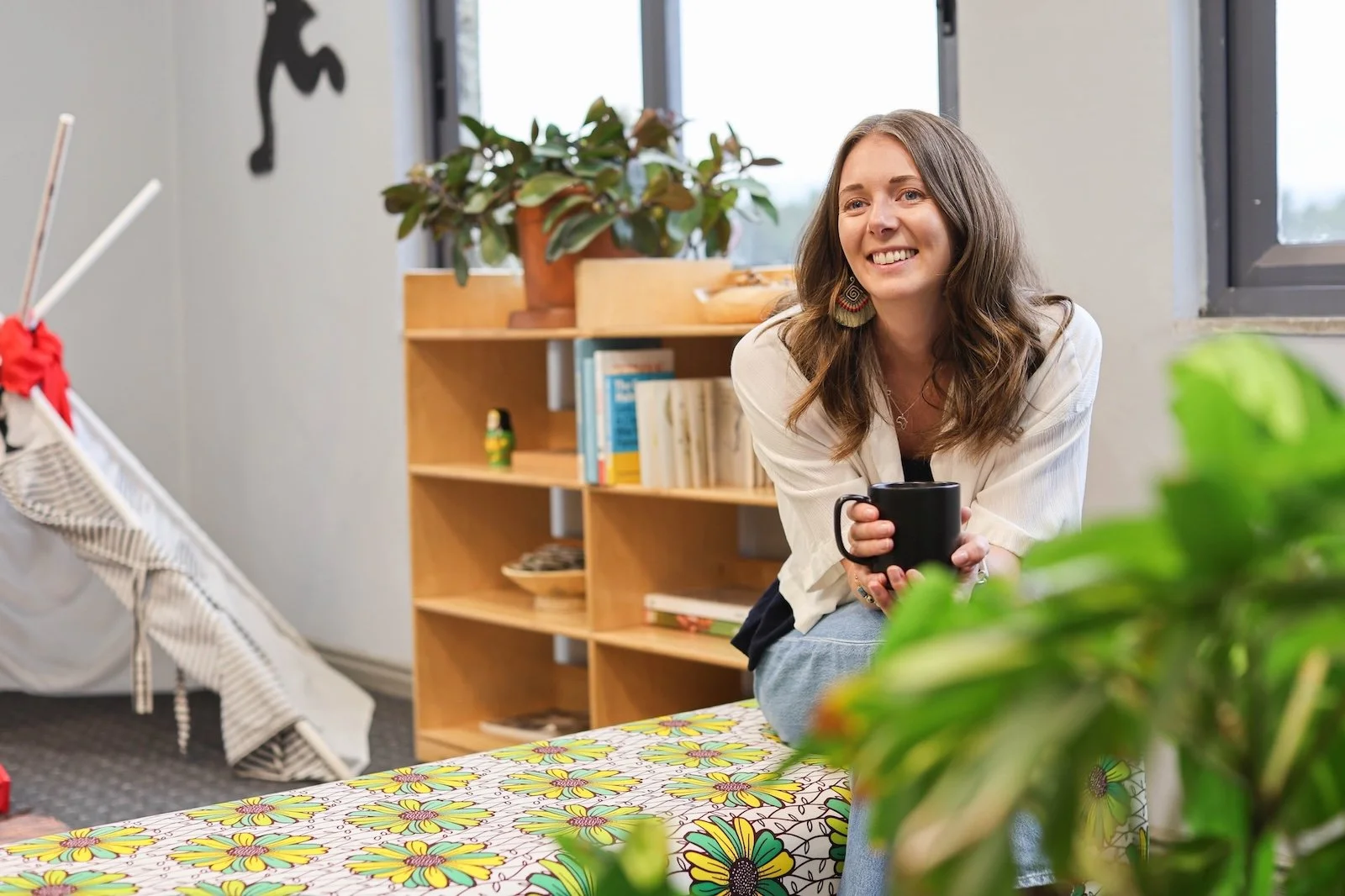 Ellie is smiling and holding a black mug. She is sitting in a cozy office.