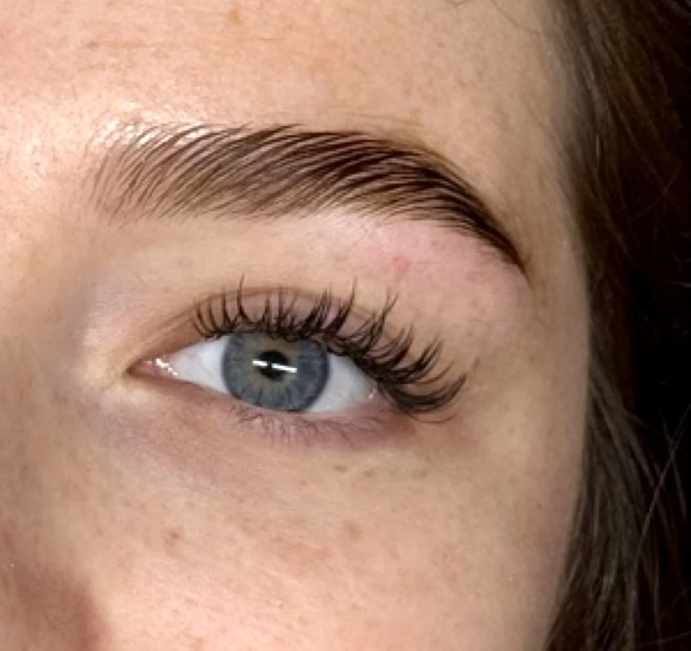 Un œil humain avec sourcils bien dessinés, cils longs et curvés, et iris bleu clair.
