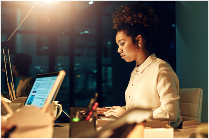 Woman working at a desk in an office during evening with city lights outside the window.