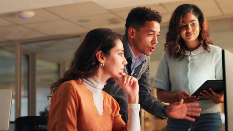 Three colleagues in an office having a discussion while looking at a computer screen.