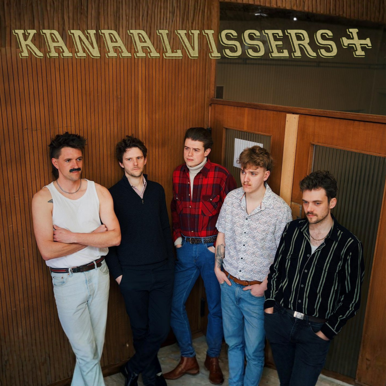 Five young men standing against a wood-paneled wall with the sign 'KANAALVISSERS' above them, wearing casual clothing and displaying various expressions.