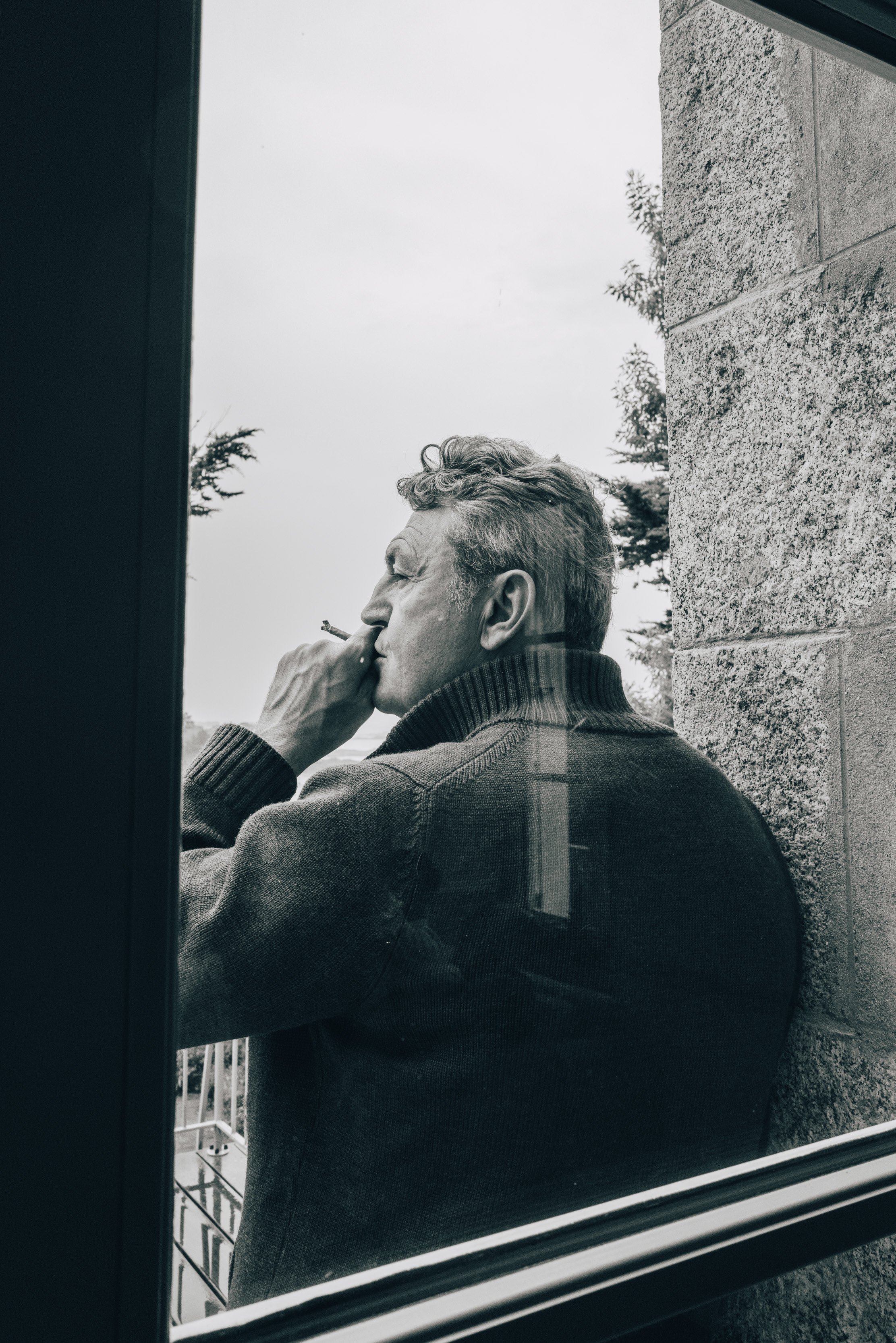 Photographie noir et blanc d'un homme âgé fumant une cigarette à la fenêtre