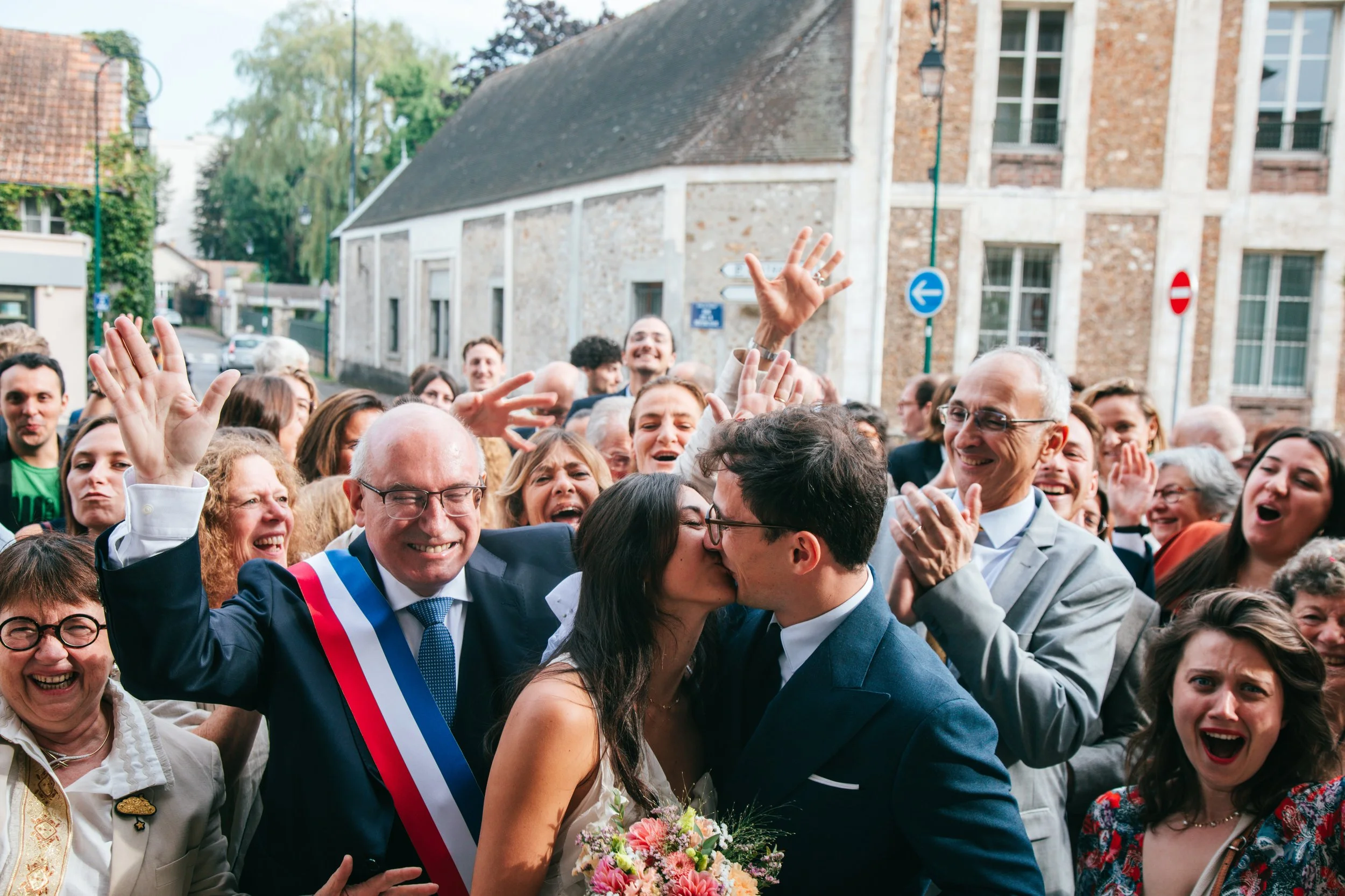 Couple de jeunes mariés s'embrassant à la sortie de la mairie entourés de leur proche
