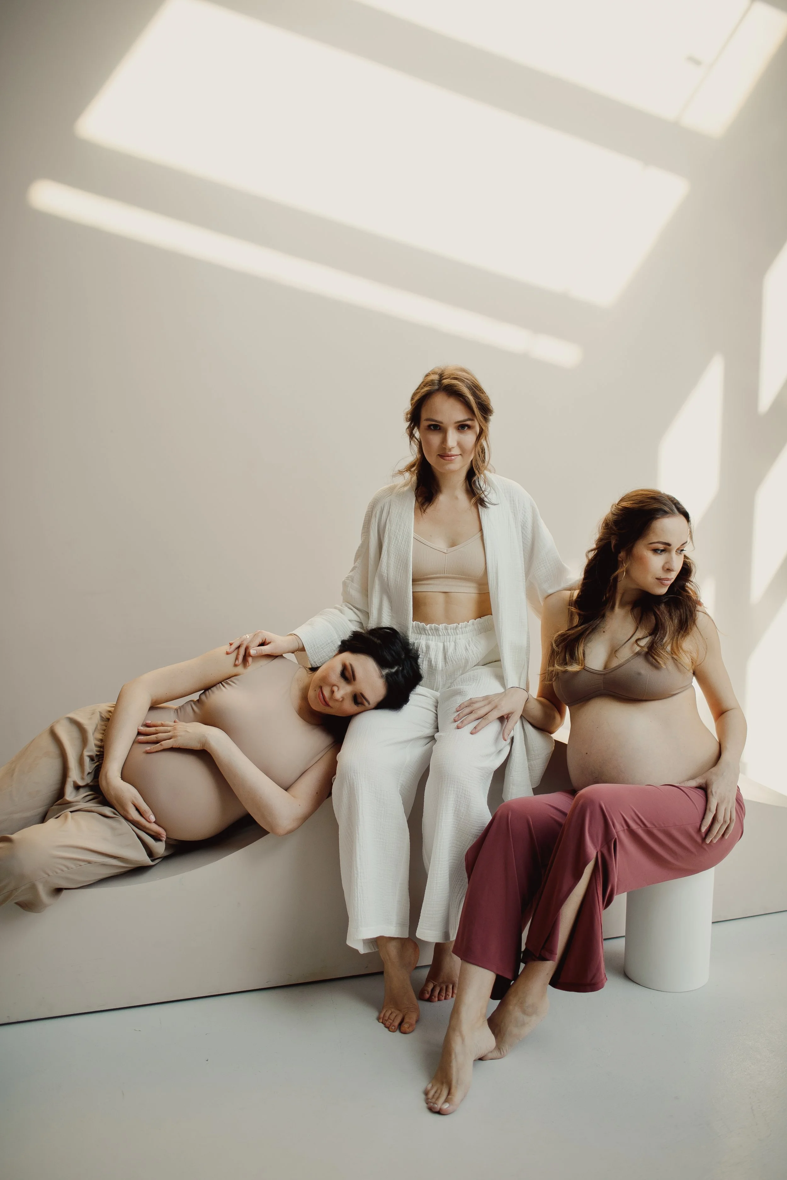 Doula with two expectant mothers relaxing together in a bright, calm room