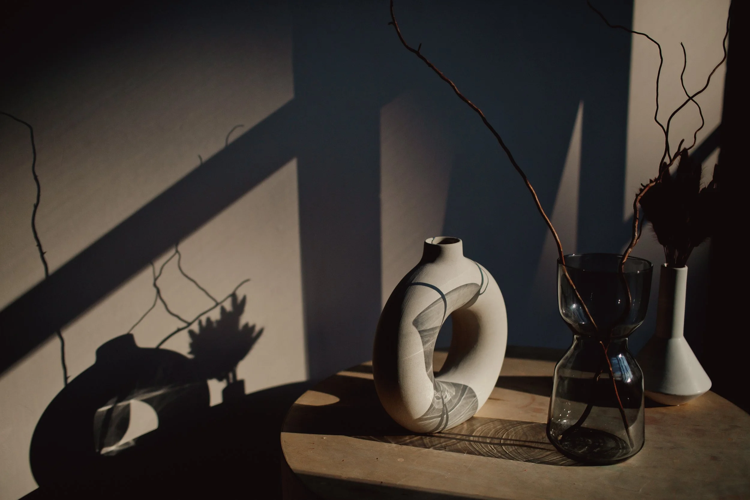 Ceramic vase and dried branches casting shadows in afternoon sun