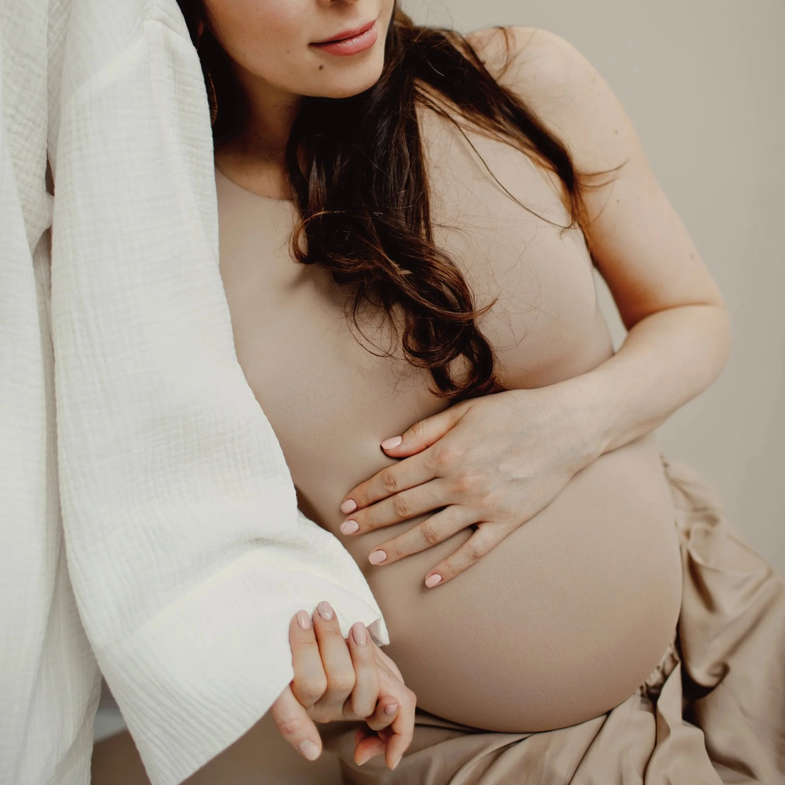 Pregnant woman in a beige bodysuit resting her hand on her belly – Classic Care doula package