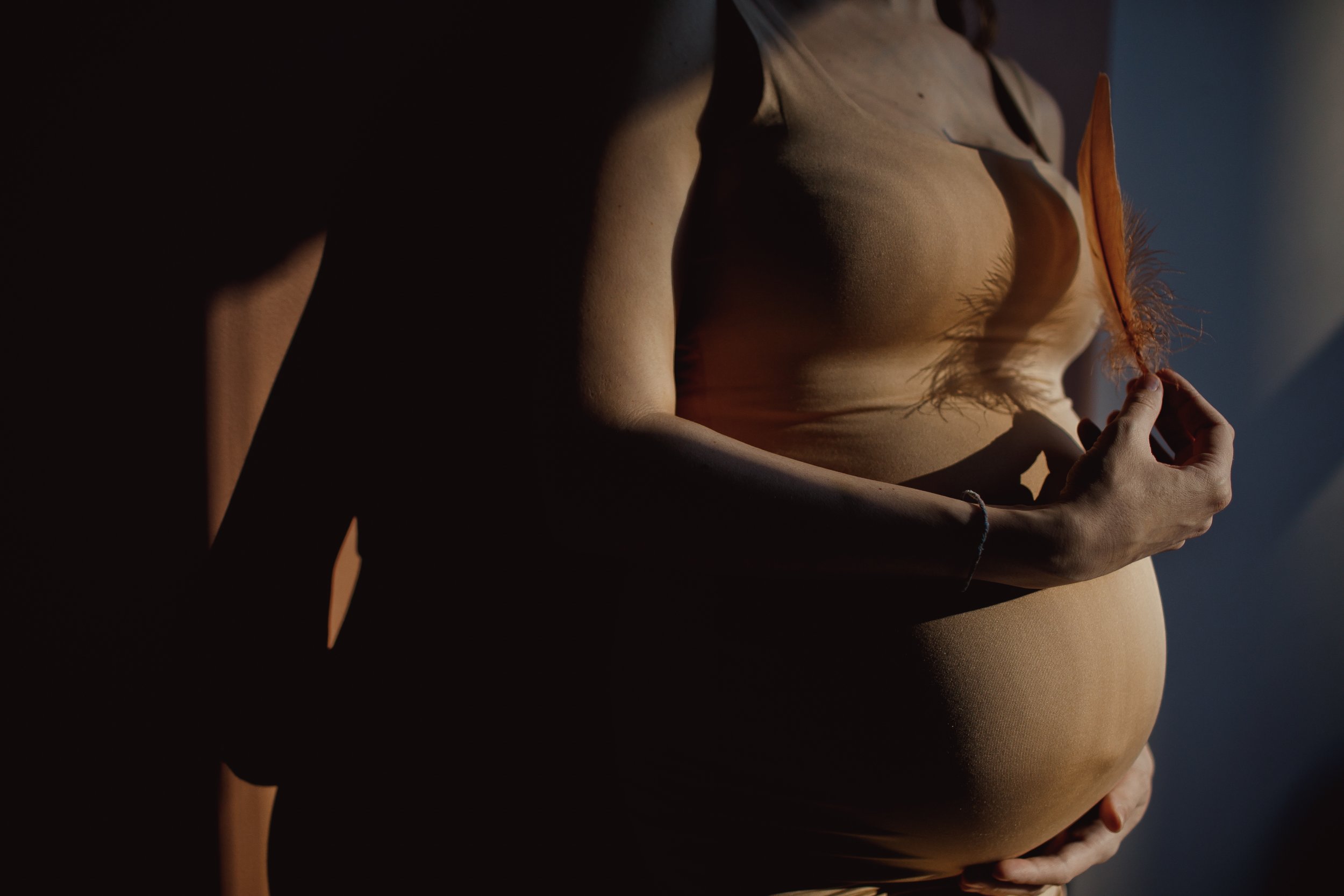 Pregnant woman cradling her belly in soft shadow – doula reading the body's cues in labor