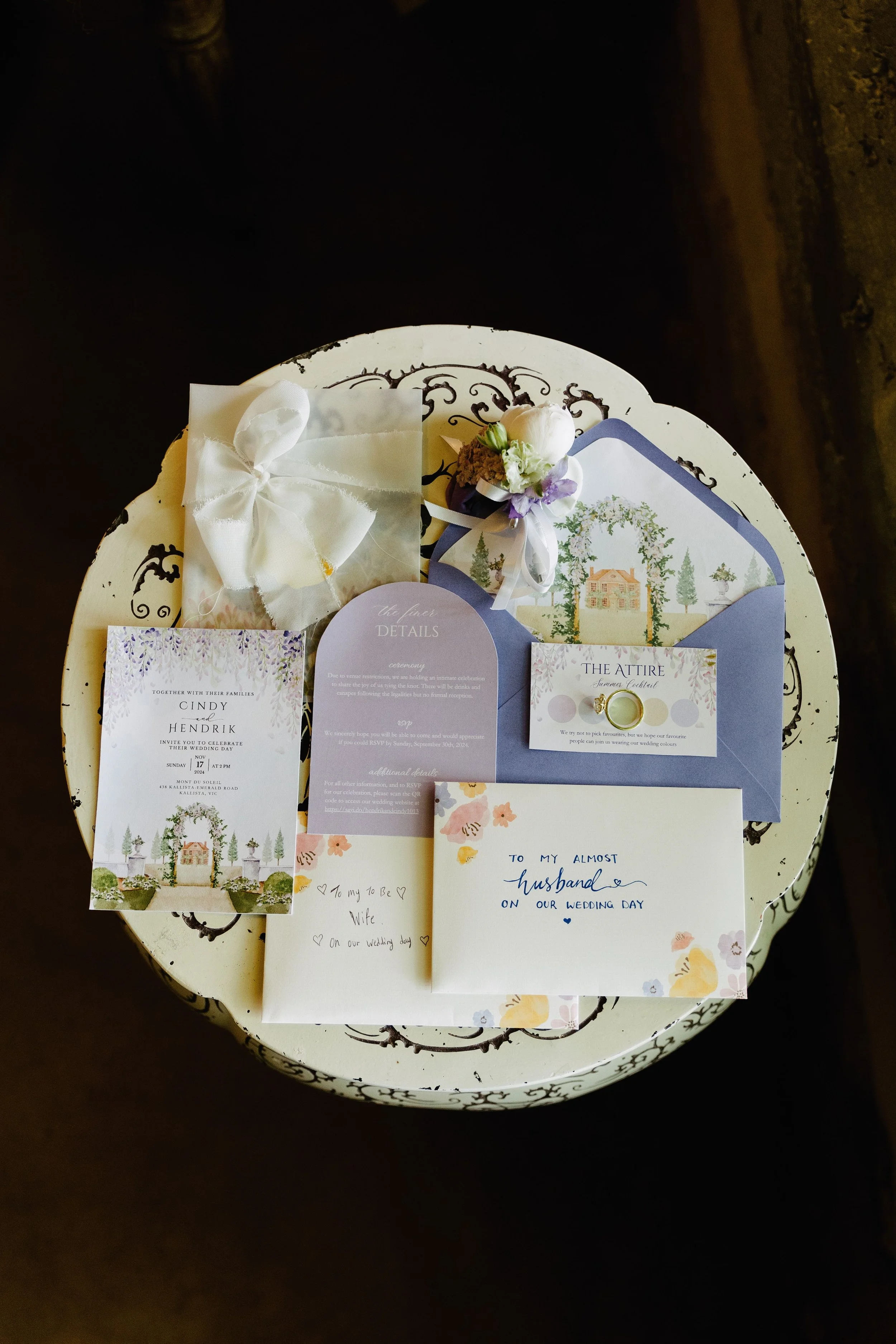 Wedding invitation suite, small flower bouquet, and handwritten note on a round, vintage-style table.