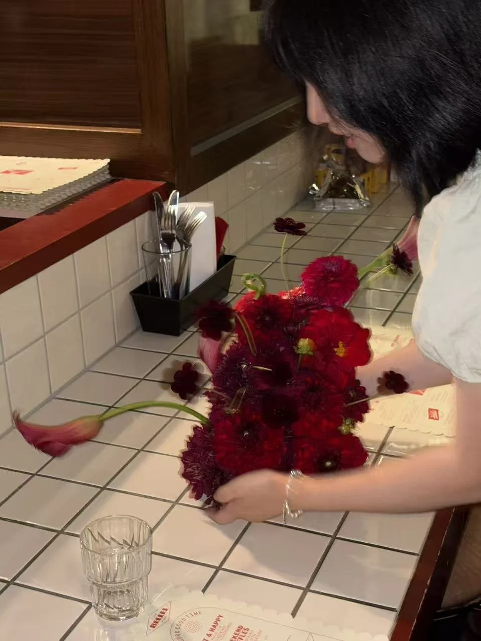 Woman arranging a bouquet of red and dark purple flowers on a tiled countertop in a birthday party.