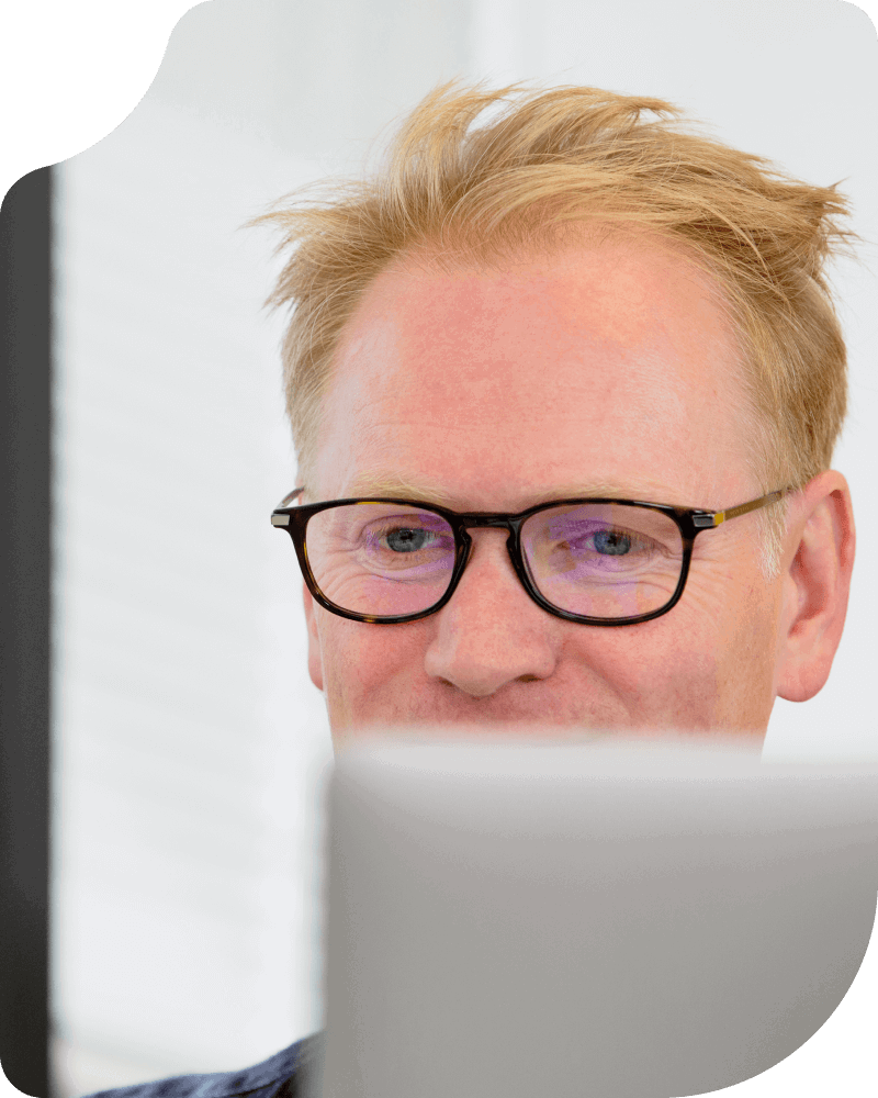 A man with blond hair, glasses, and fair skin is looking at a computer screen.