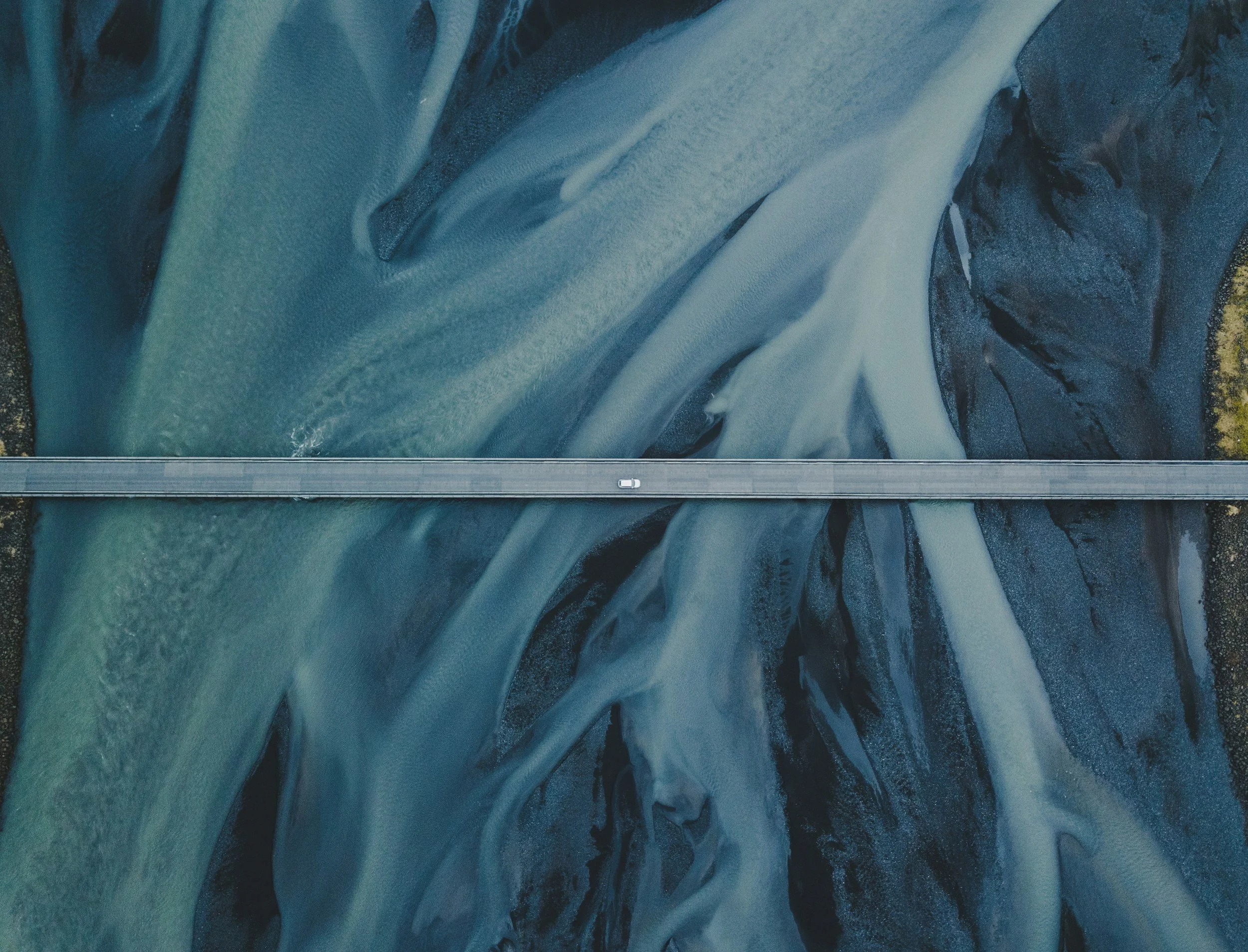 Overhead view of a winding river with dark and light blue waters surrounded by dark rocks and terrain.