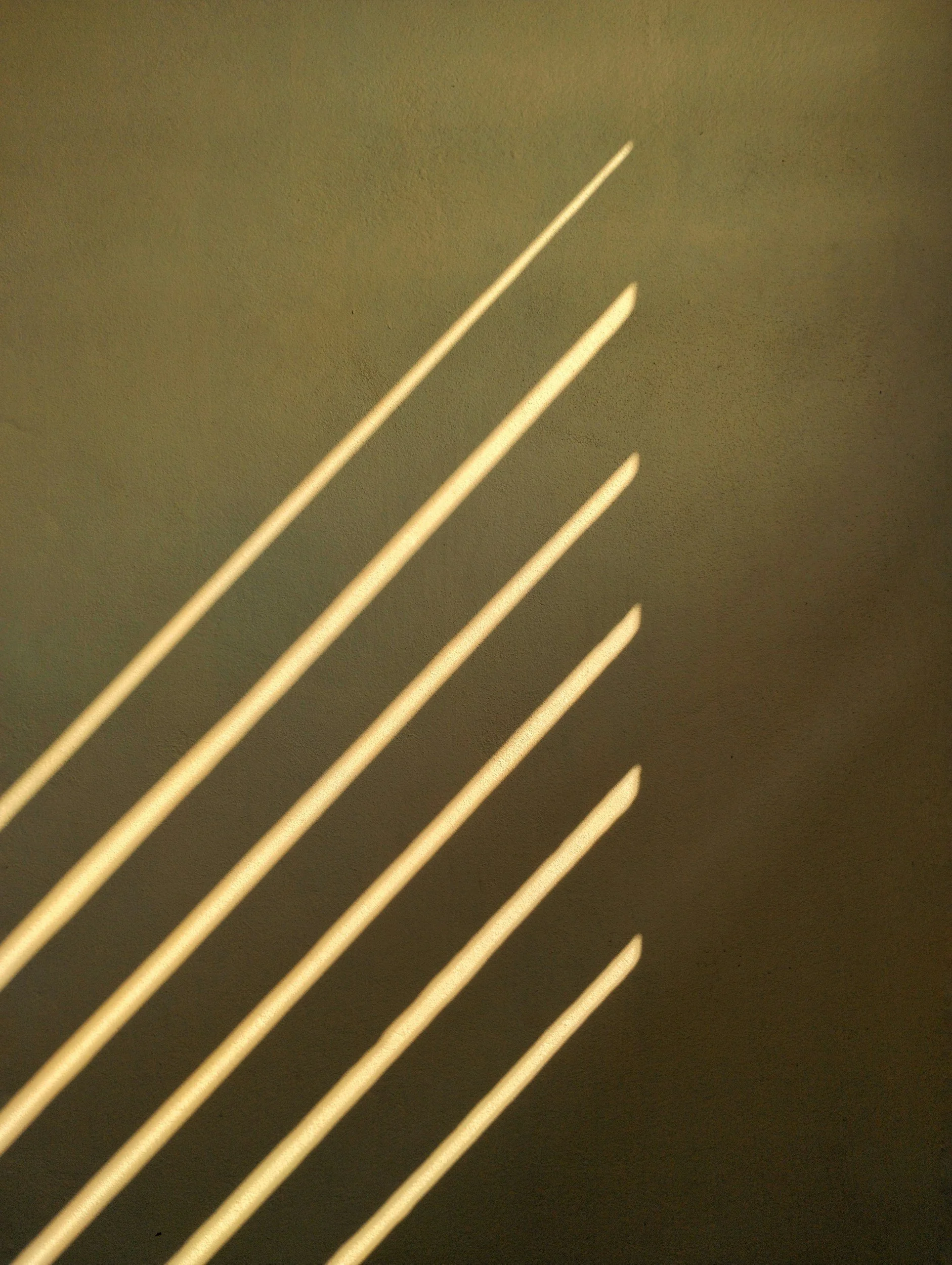 Close-up of sharp, curved metal prongs casting shadows on a plain, light-colored wall.