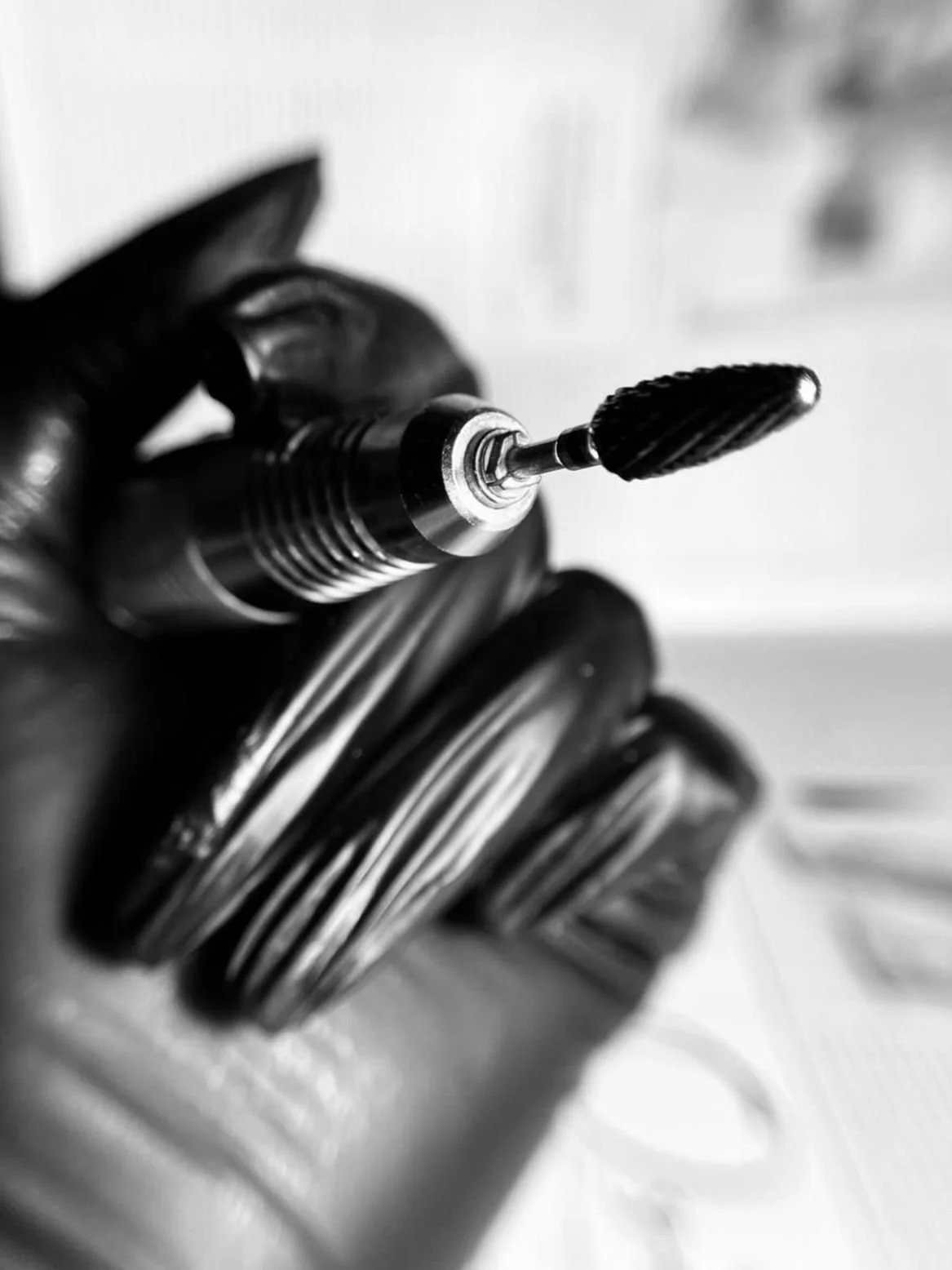 Schwarz-weiß-Foto eines Bohrers, der in eine Maschine eingespannt ist, mit einem Handstück mit rillenförmigem Design, in einer Werkstatt oder im technischen Umfeld.