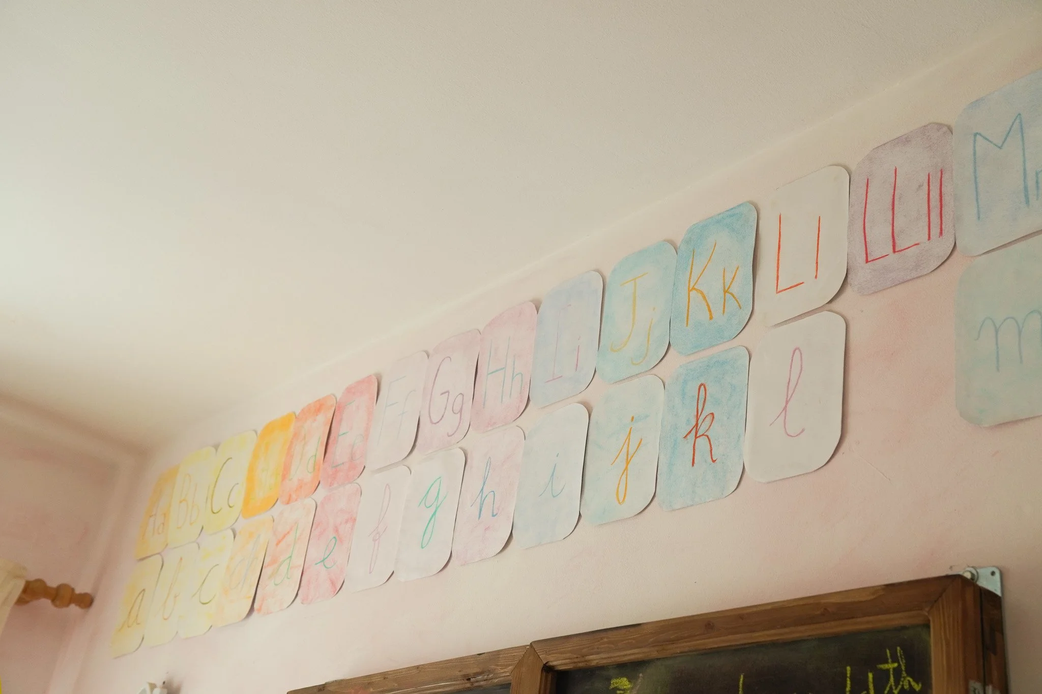 Carteles de papel con letras del alfabeto en diferentes colores y estilos escritos a mano, pegados en una pared.