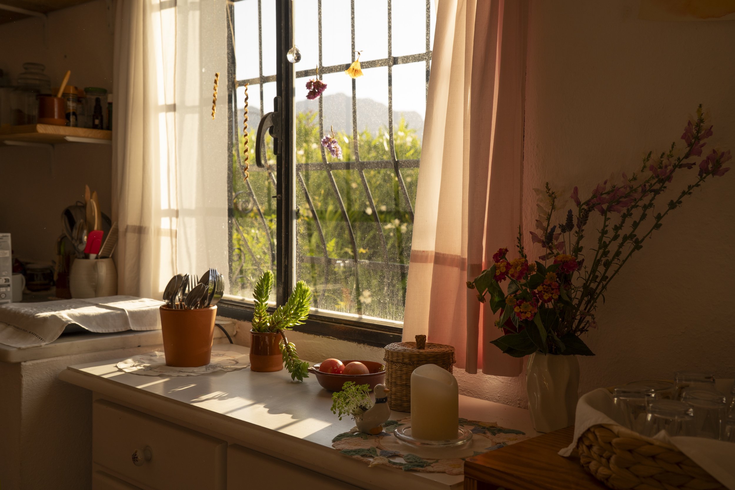 Vista de una cocina con ventana, flores, plantas y velas en una mesa