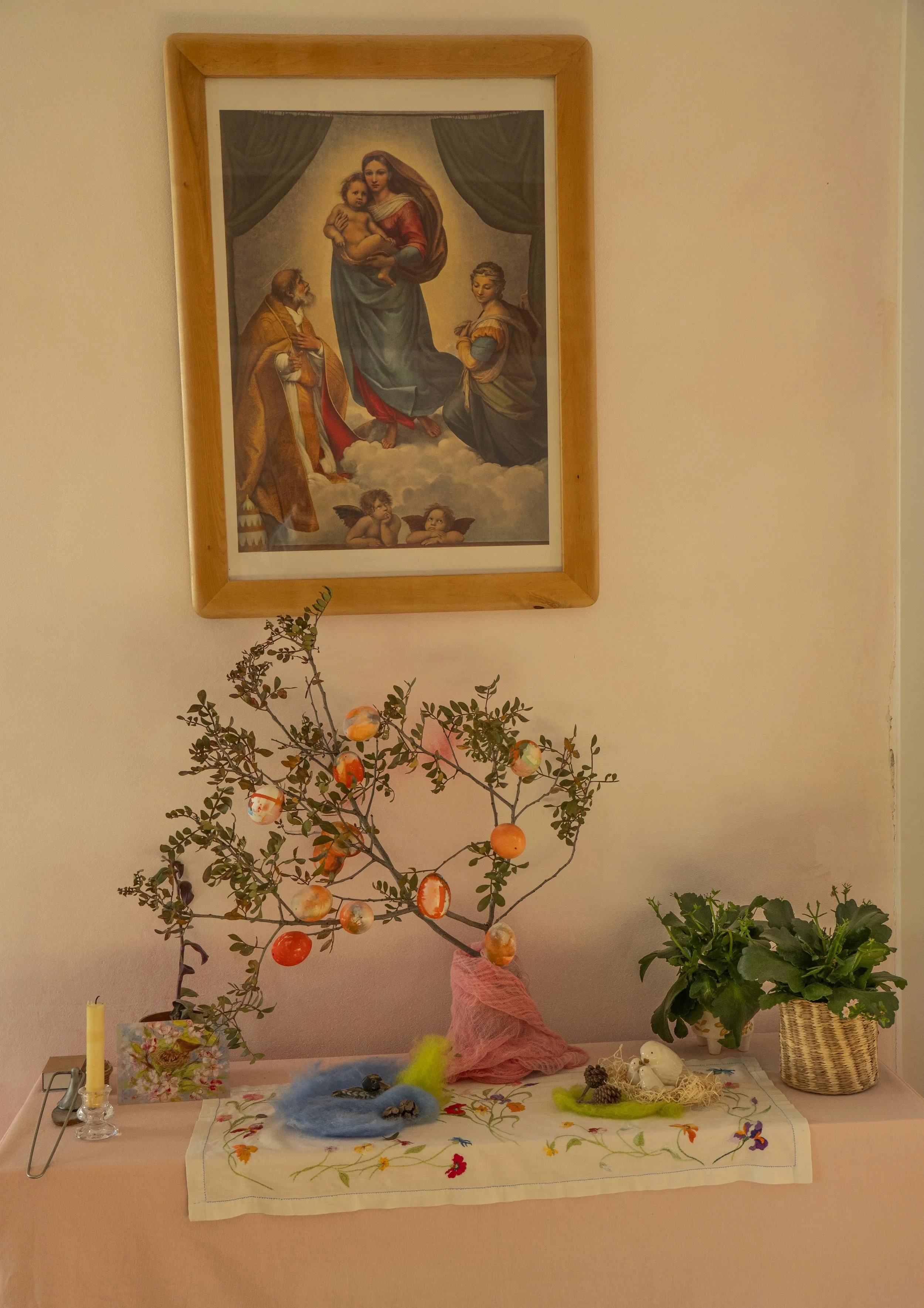 Mesa con decoración festiva, un árbol con adornos, objetos decorativos, y un cuadro religioso en la pared.