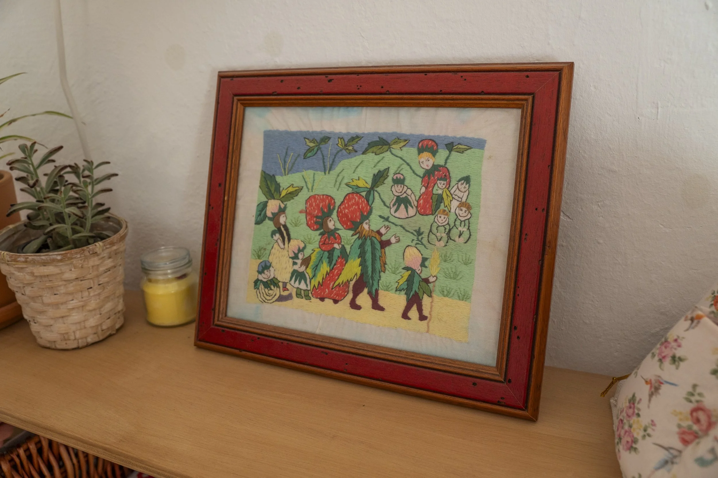 Cuadro con dibujos coloridos de personas y plantas en un marco de madera rojo en una habitación.