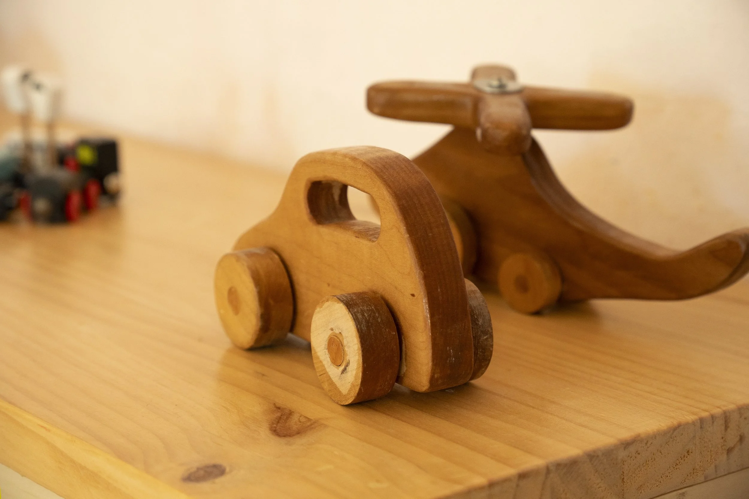 Juguetes de madera en forma de vehículo y avión en una mesa de madera.