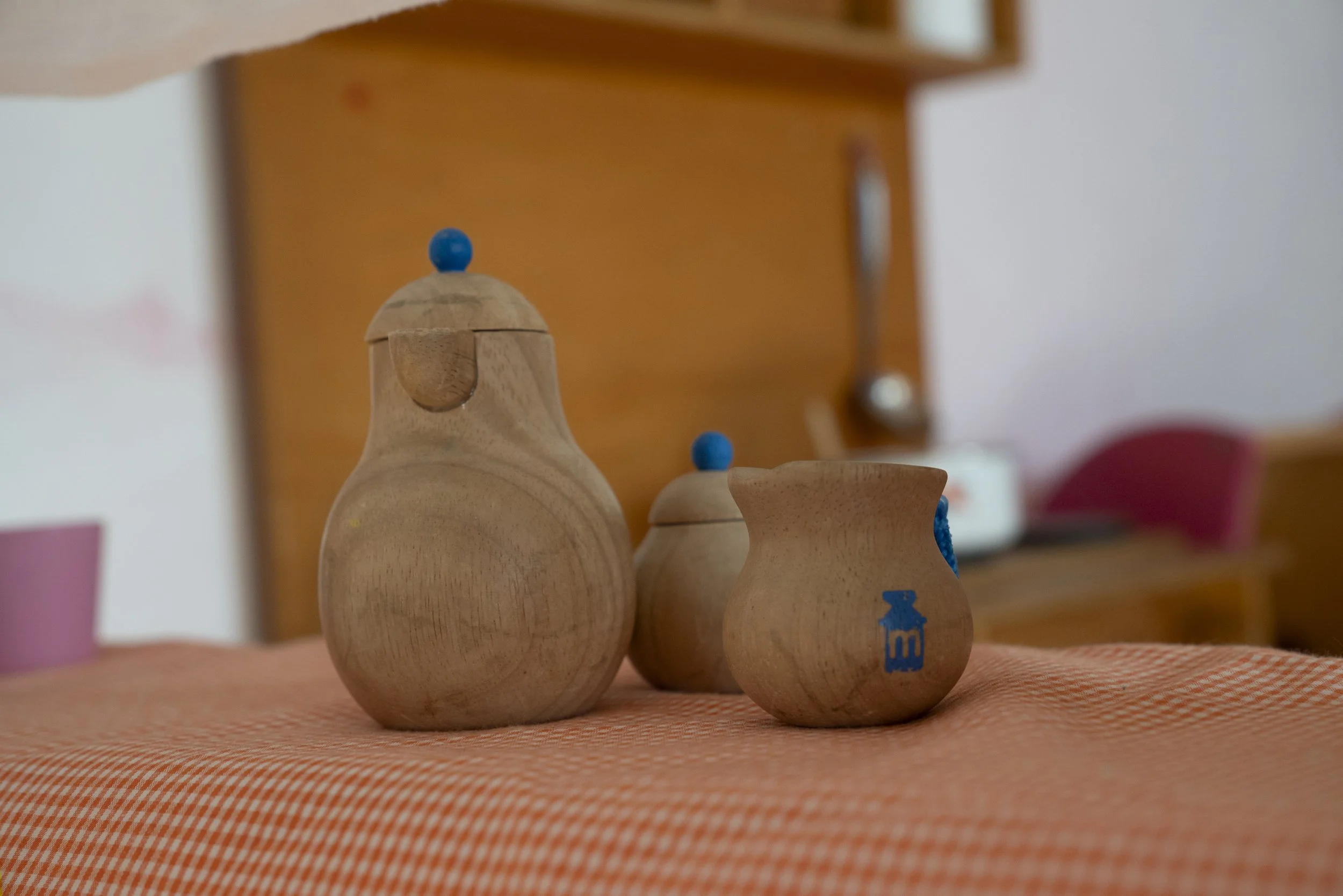 Diversas piezas de madera en forma de frascos o vasijas con algunos decorados en azul, colocadas sobre una mesa cubierta con un mantel a cuadros en tonos naranja.