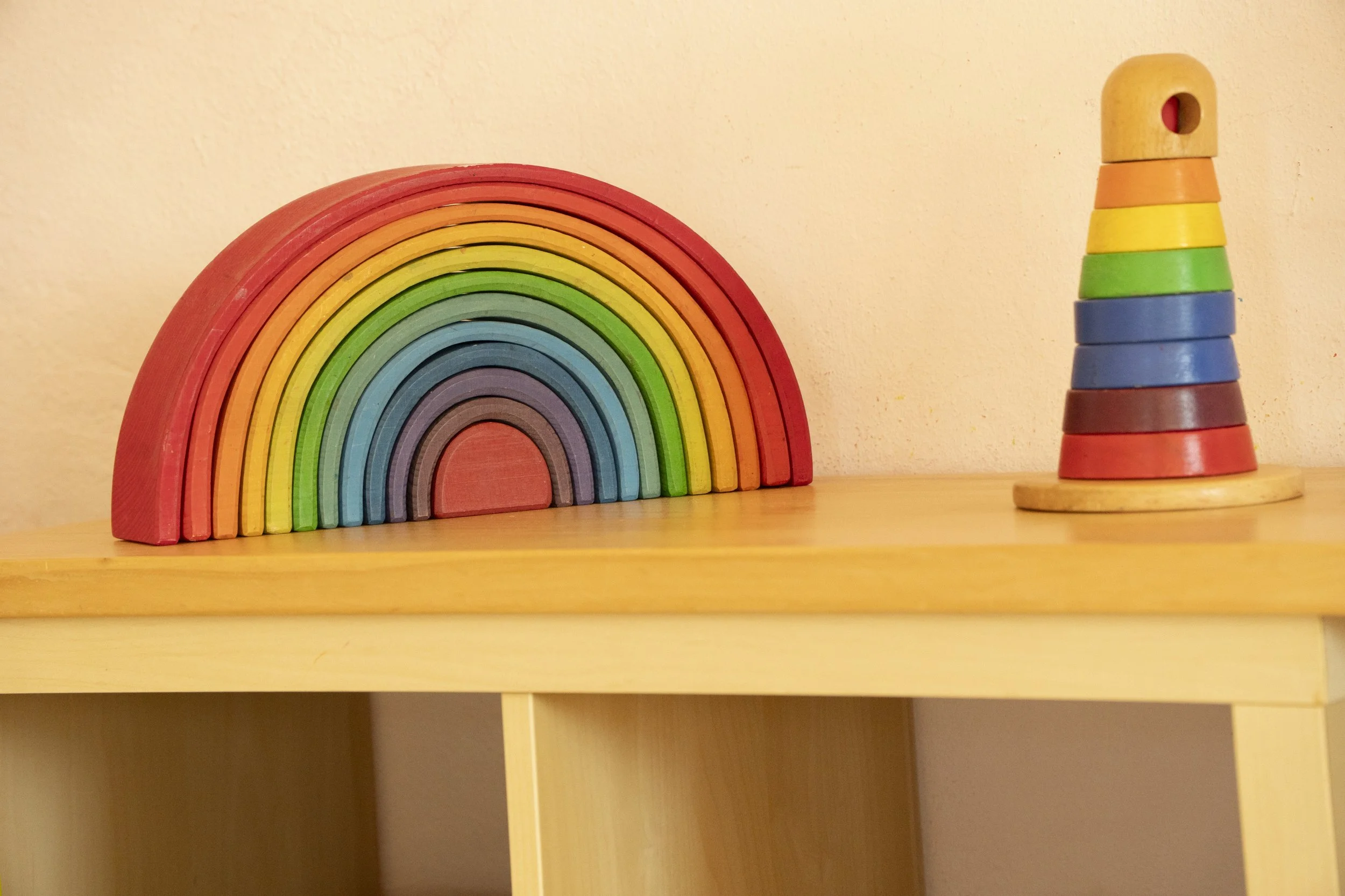 Conjunto de bloques de madera apilados formando un arcoiris y una torre de colores sustentada en una superficie de madera.