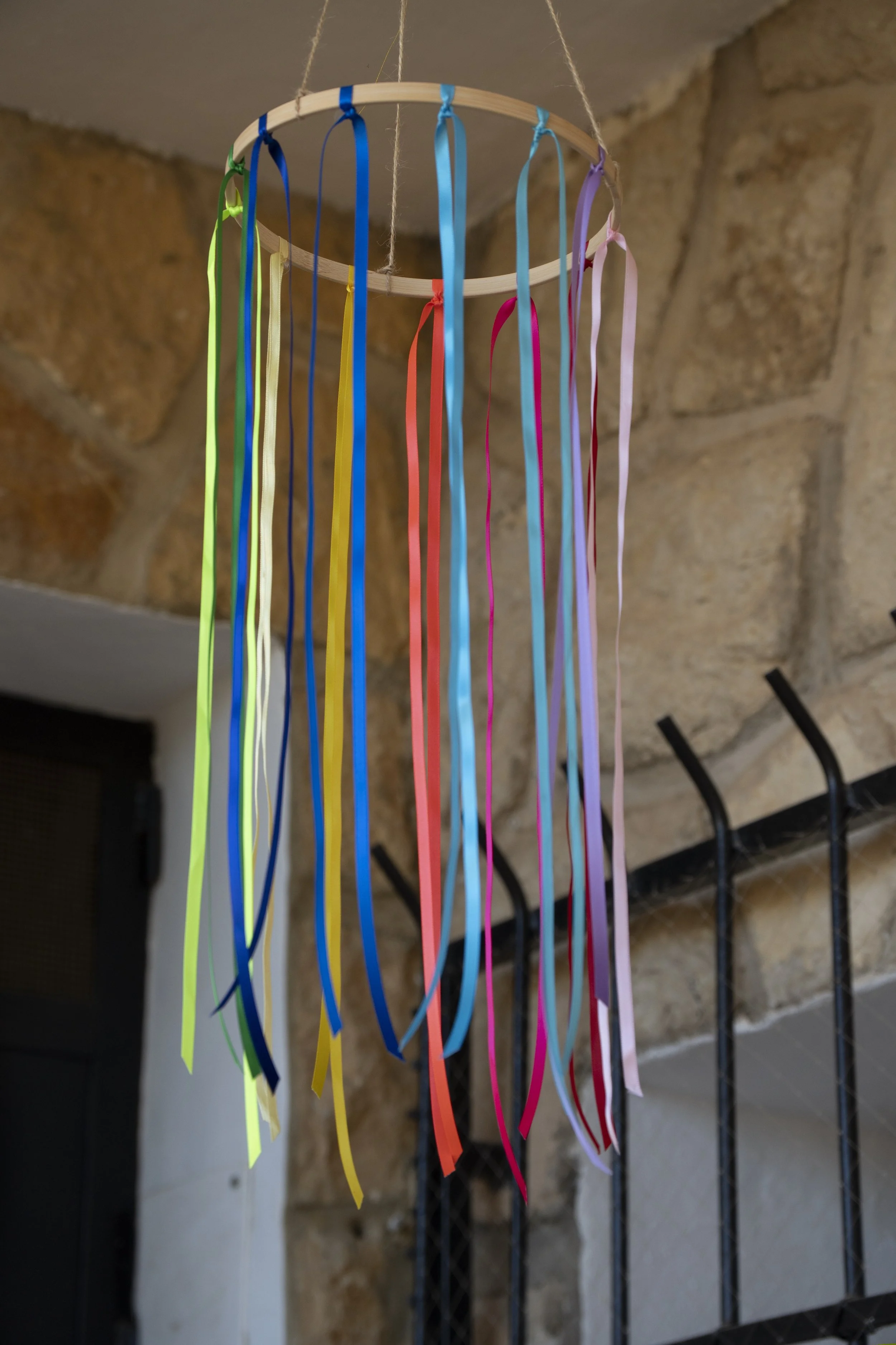 Campana decorativa con cintas de colores colgada del techo, en un fondo de paredes de piedra.