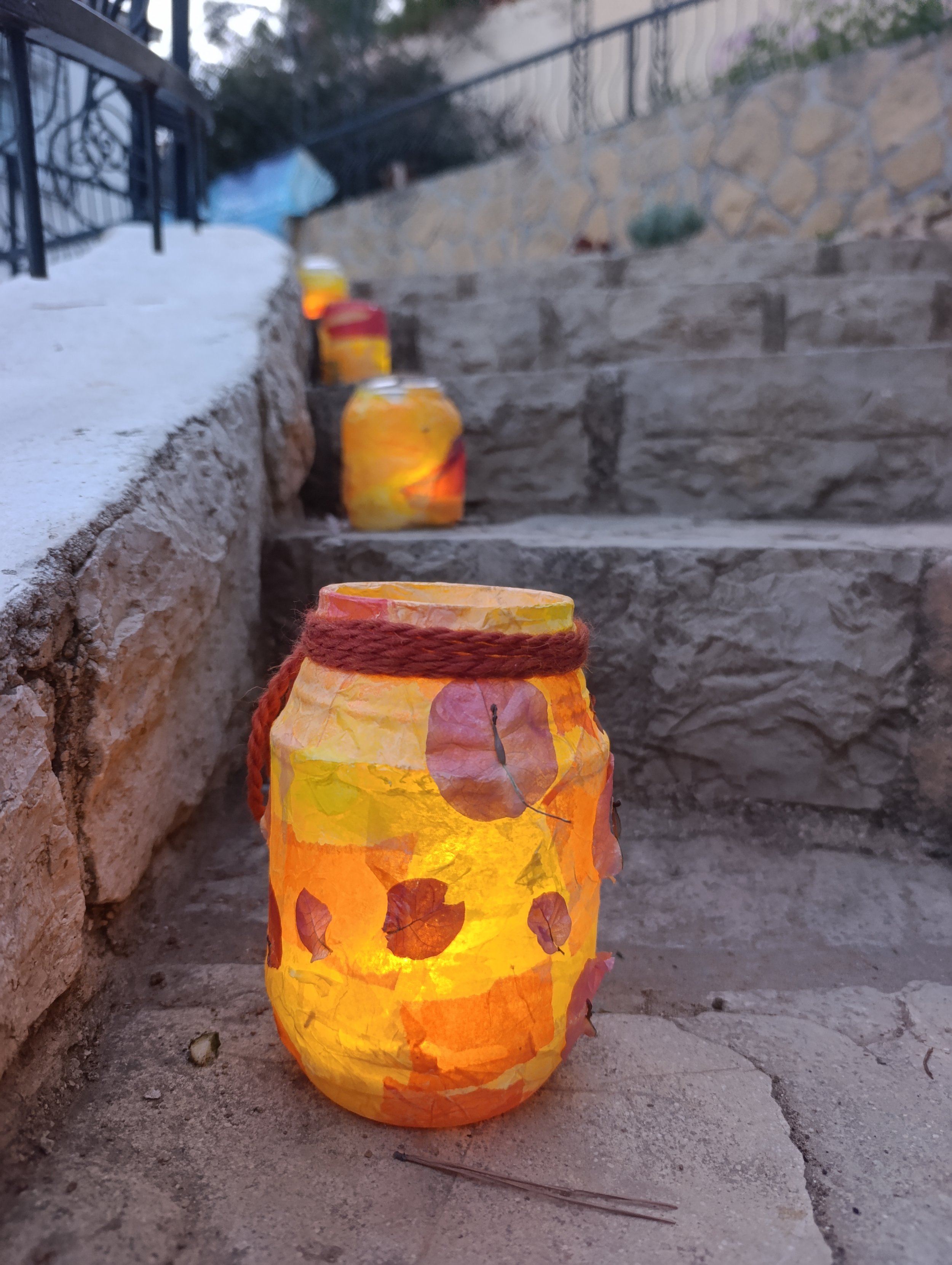 Farol de papel decorado con hojas secas, iluminado, en una escalera de piedra en un espacio al aire libre.