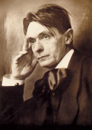 Retrato en sepia de un hombre con cabello oscuro, vestido con traje y corbata, con expresión pensativa, tocándose la cabeza con la mano derecha.