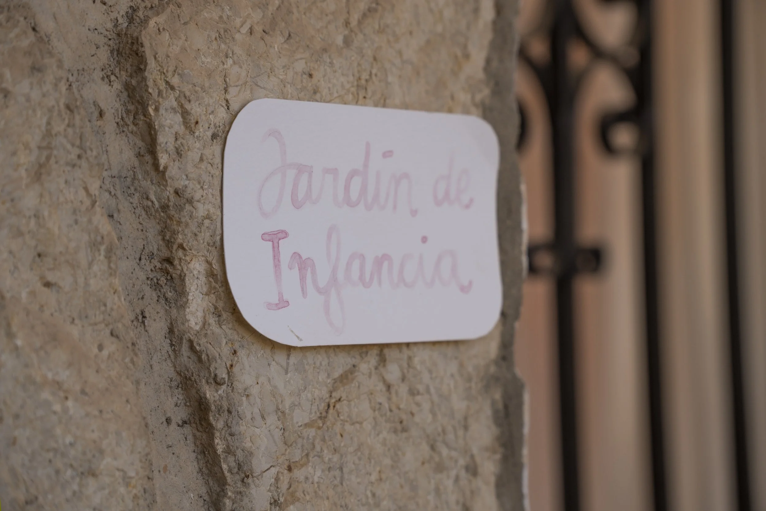 Etiqueta en la pared que dice 'Jardín de Ivana' escrita a mano en tinta color rosa, colocada en una pared de piedra.