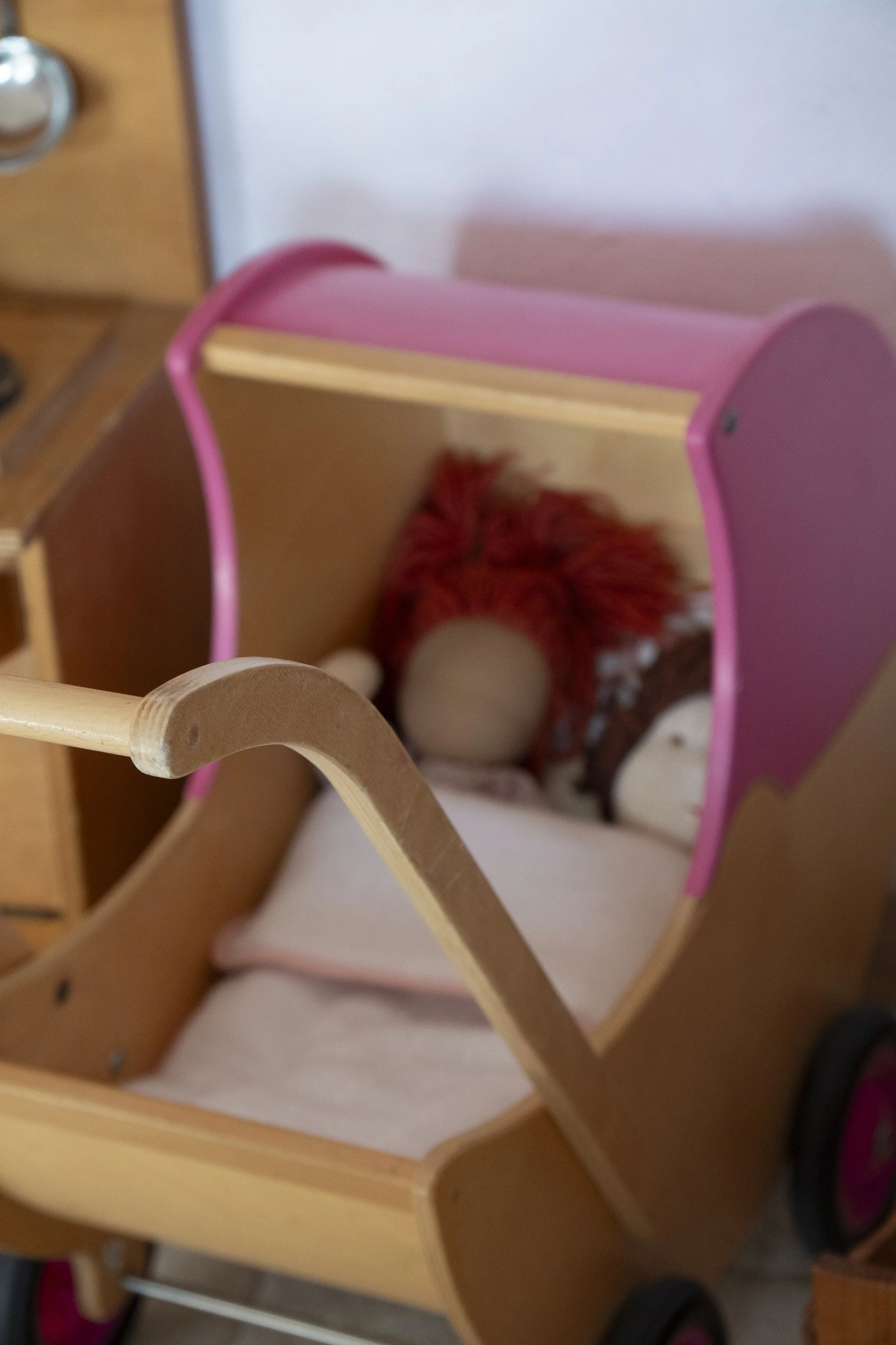 Una carriola de madera y plástico rosa, con juguetes dentro, en una habitación