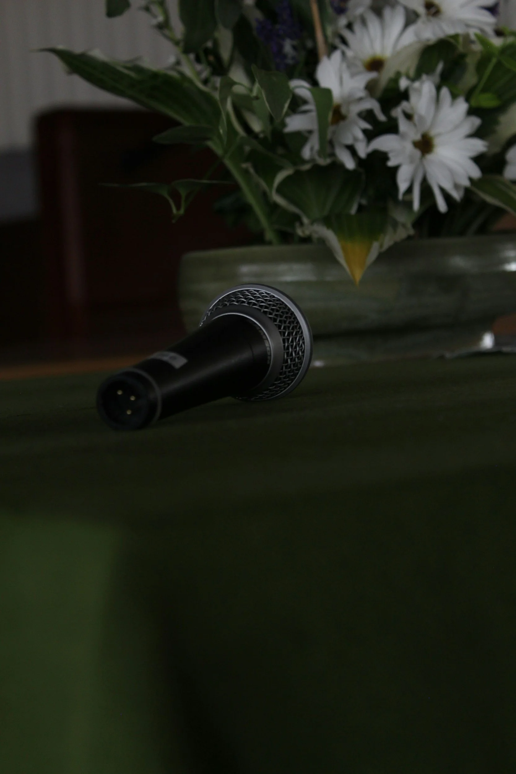 Close-up of a microphone with a bouquet of white flowers and green leaves in the background.