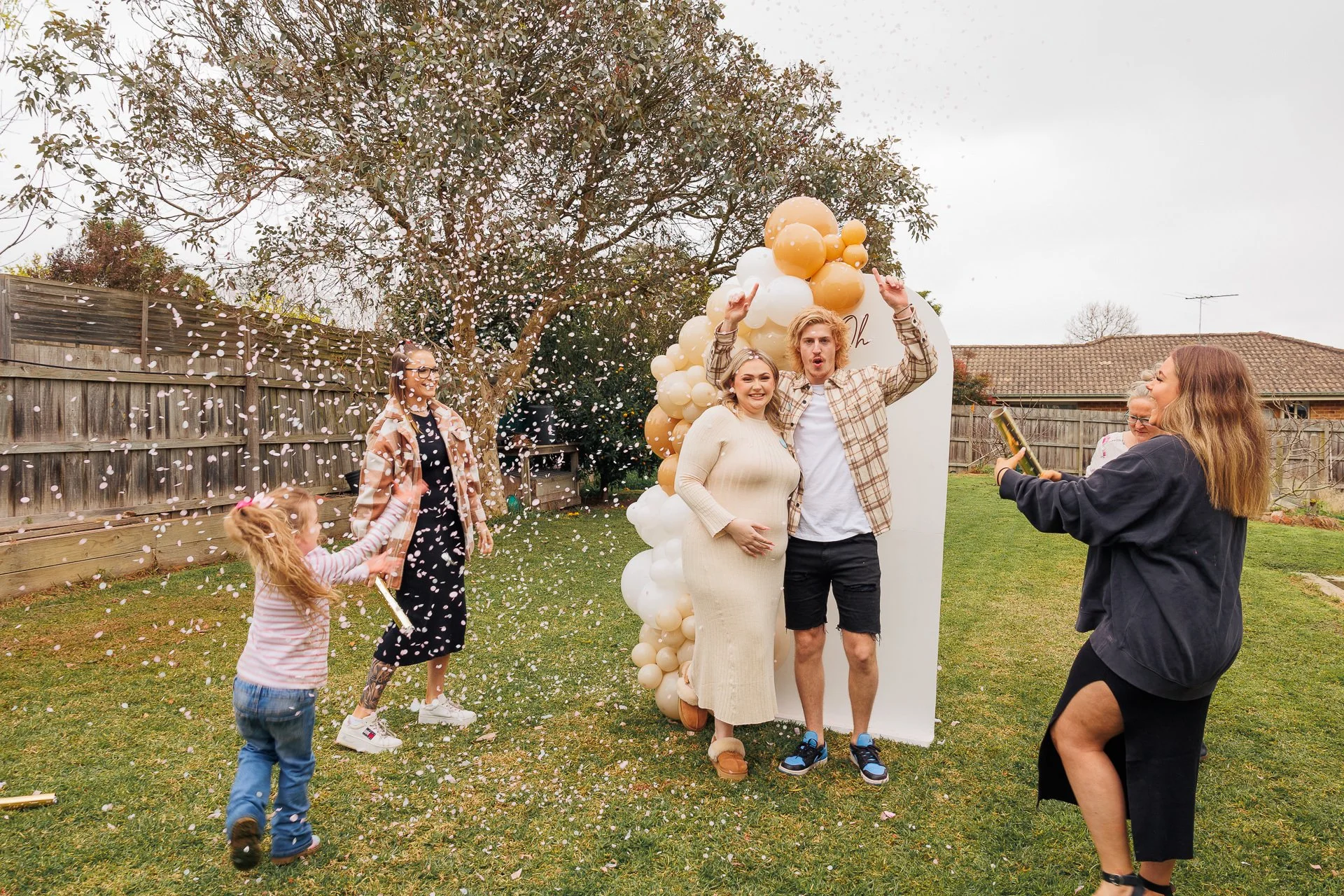 Family celebrating a gender reveal in a backyard with balloons and confetti.