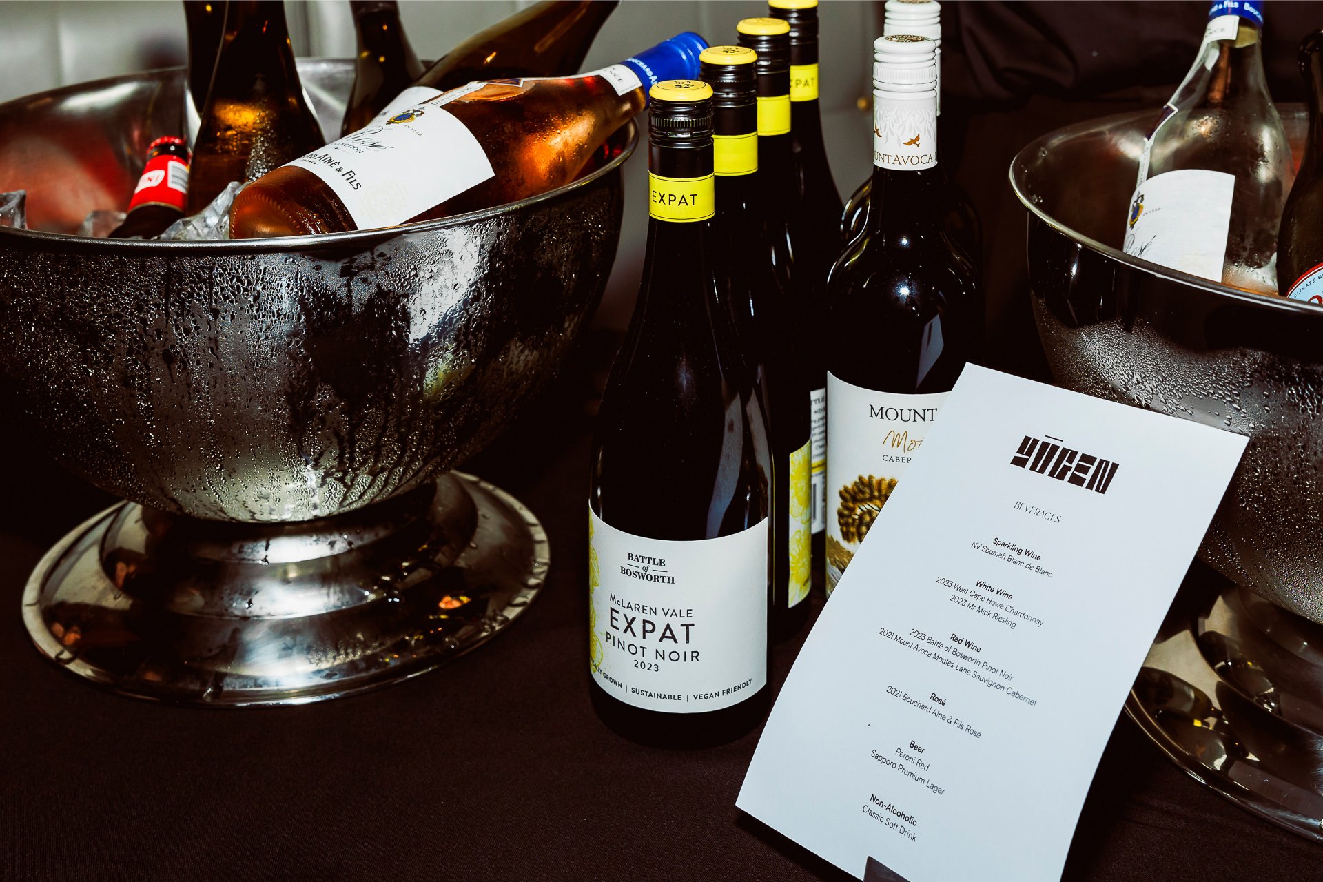 Bottles of wine in ice buckets and a menu at a wine tasting event.