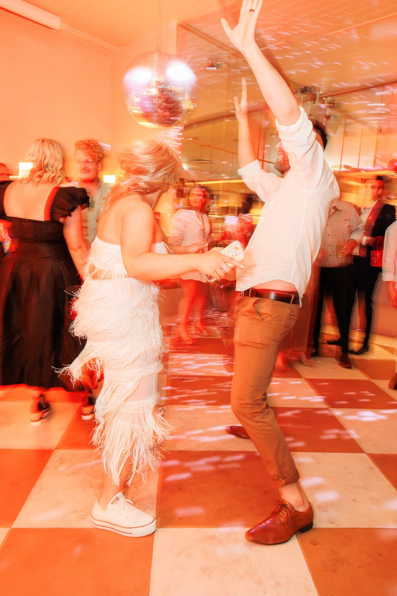 People dancing in a lively party with a disco ball and colorful lighting.