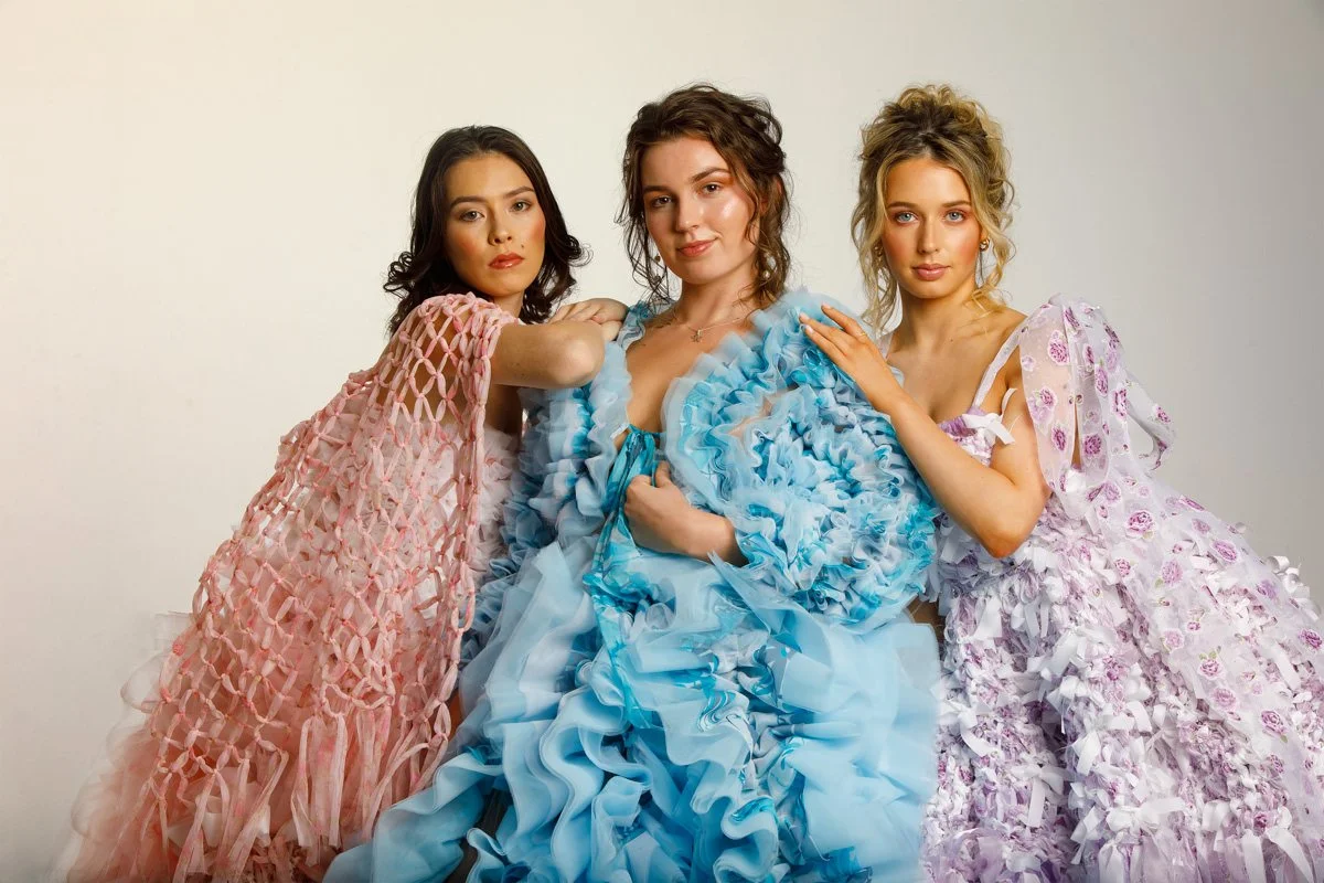 Three women dressed in elaborate, colorful dresses posing together against a plain background.