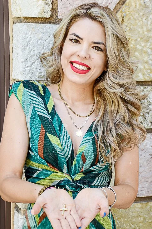 Χαμογελαστή νονά δείχνει τον χρυσό βαπτιστικό σταυρό στις παλάμες της. Επαγγελματίας φωτογράφος βάπτισης για κάλυψη λεπτομερειών.