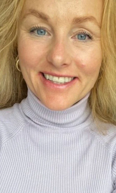 Portræt af en smilende kvinde med blonde hår, blå øjne og iført en lysegrå turtleneck.