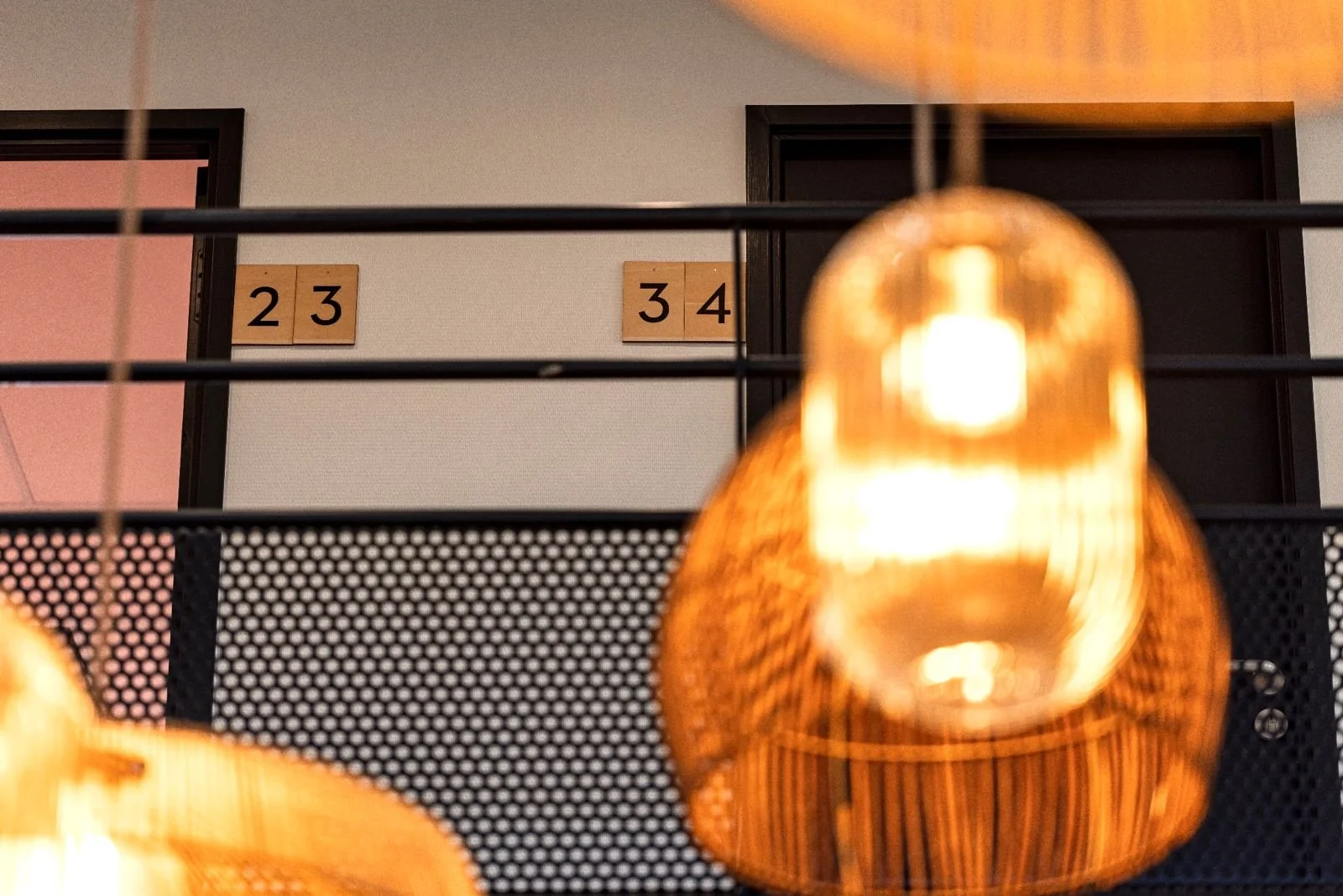 Vue intérieure d'un espace avec deux portes affichant les numéros 23 et 34, décor moderne avec lampes suspendues en rotin éclairant doucement.
