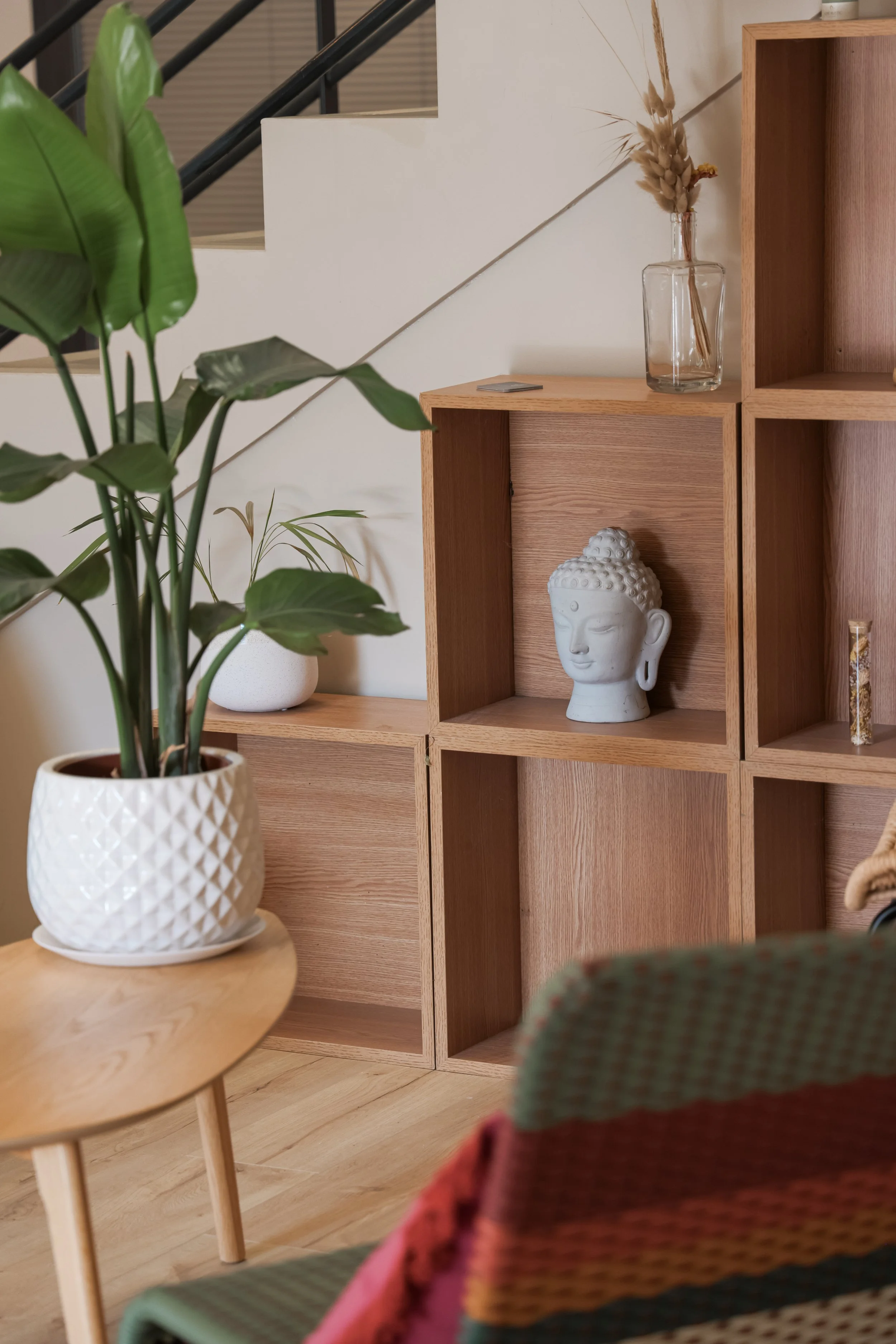 Une étagère en bois avec une sculpture de Bouddha blanche, une bouteille en verre avec des fleurs séchées, et une petite plaque ou un livre.