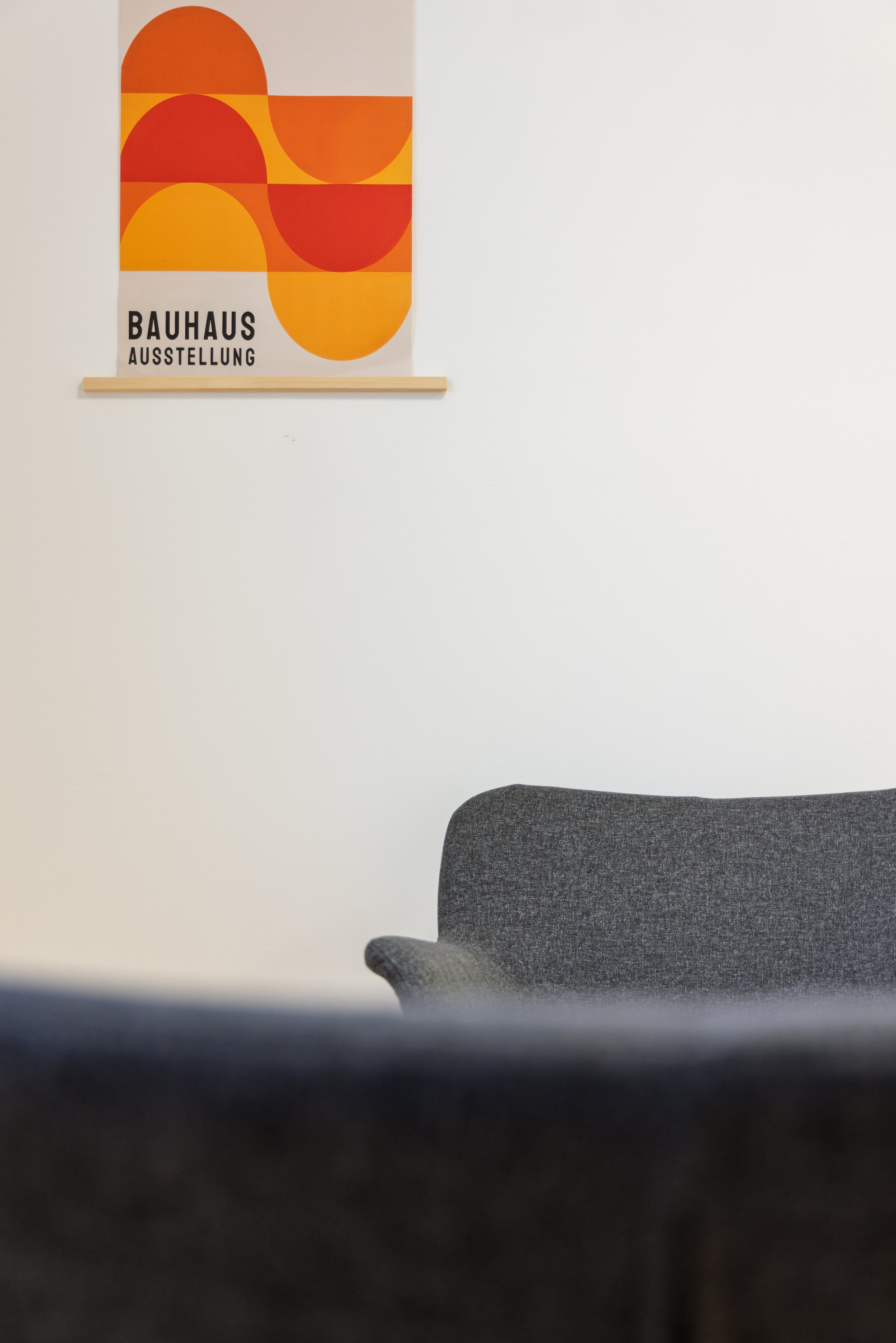 Une affiche colorée avec des formes géométriques oranges, rouges et jaunes, affichée sur un mur blanc, avec le texte 'BAUHAUS AUSSTELLUNG' en bas à gauche.