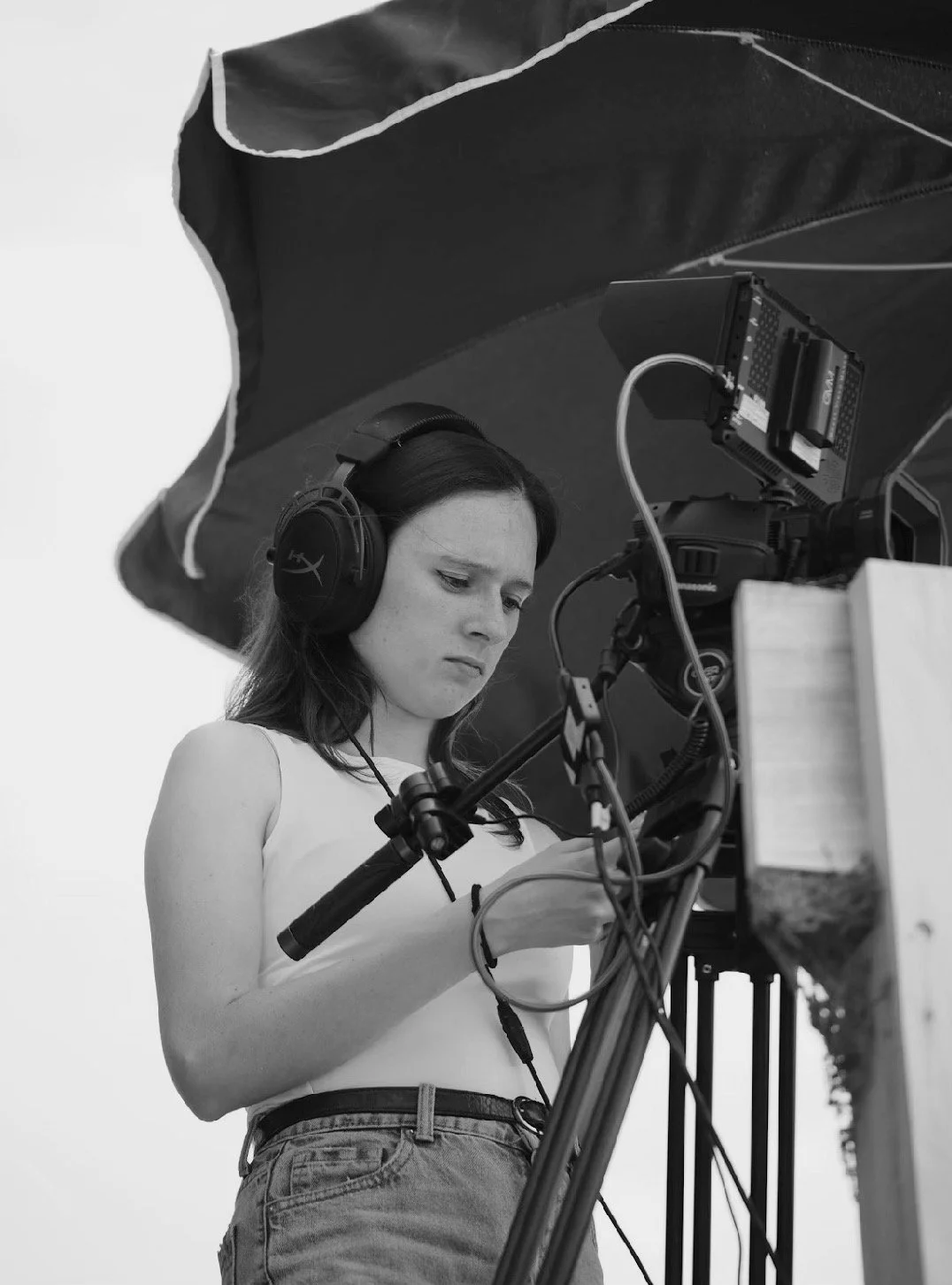 Femme brune concentrée en train de filmer avec une caméra et un casque audio, en noir et blanc