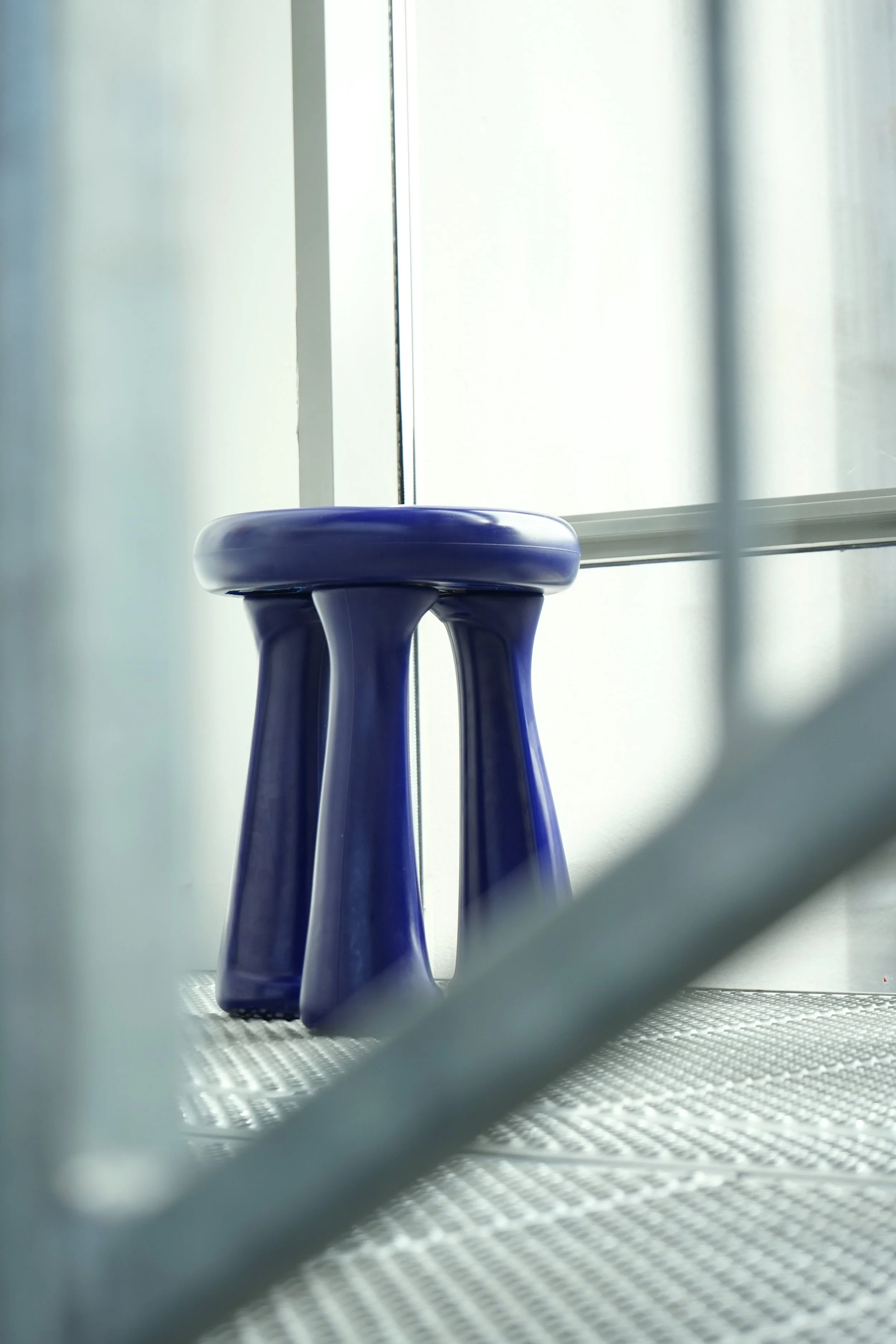 Close-up of three purple plastic stools in front of a window, taken from a low angle with a blurred foreground.