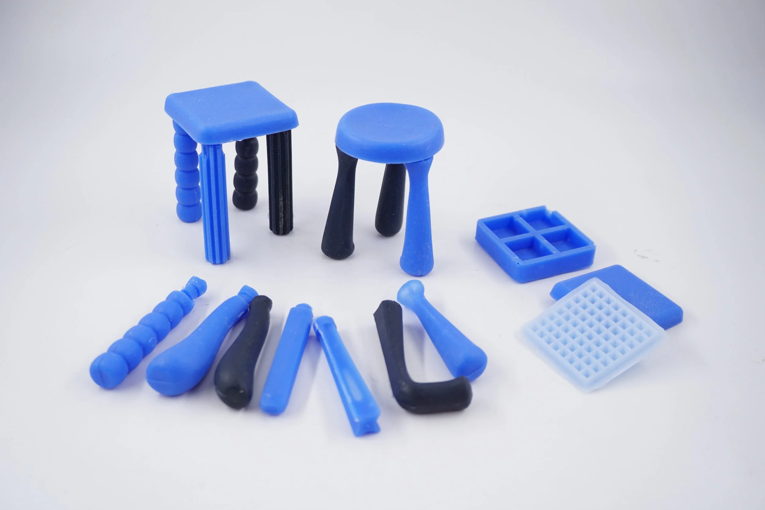 Various small blue and black plastic objects on a white surface, including miniature stools, tools, and storage containers.