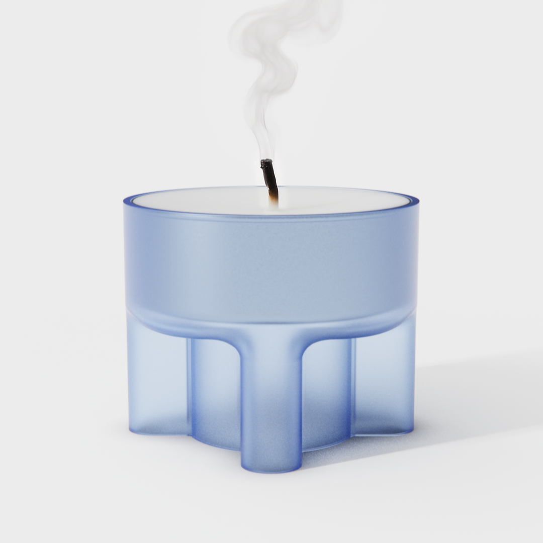 A blue candle with a black wick that is burning and producing a small amount of smoke, set against a plain white background.