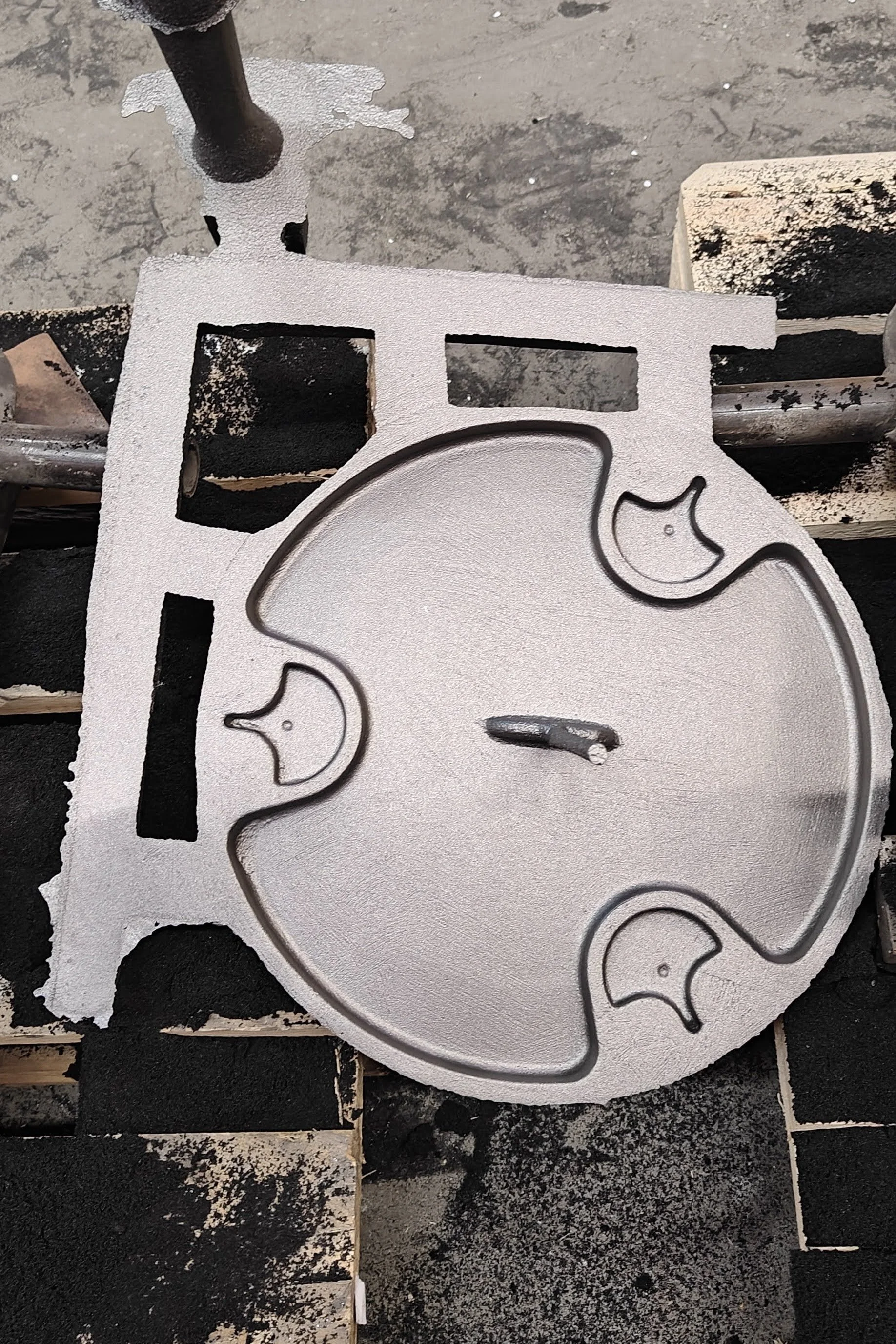 A metal cutout with elephant shapes on a black and white surface, with parts of the surrounding area showing bare ground and a stone block.